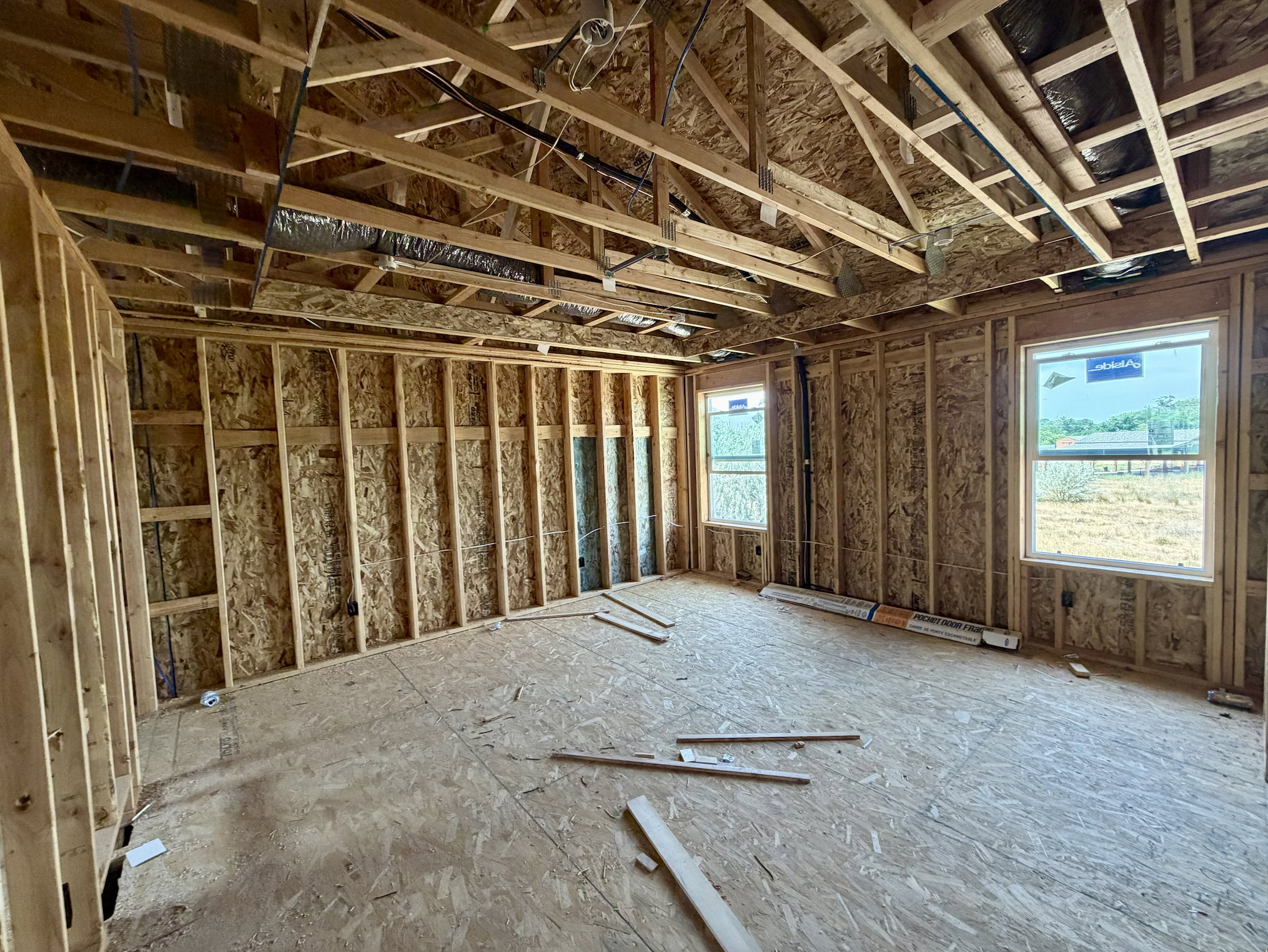 New construction framing featuring two windows, exposed ceiling joists, and plywood subflooring