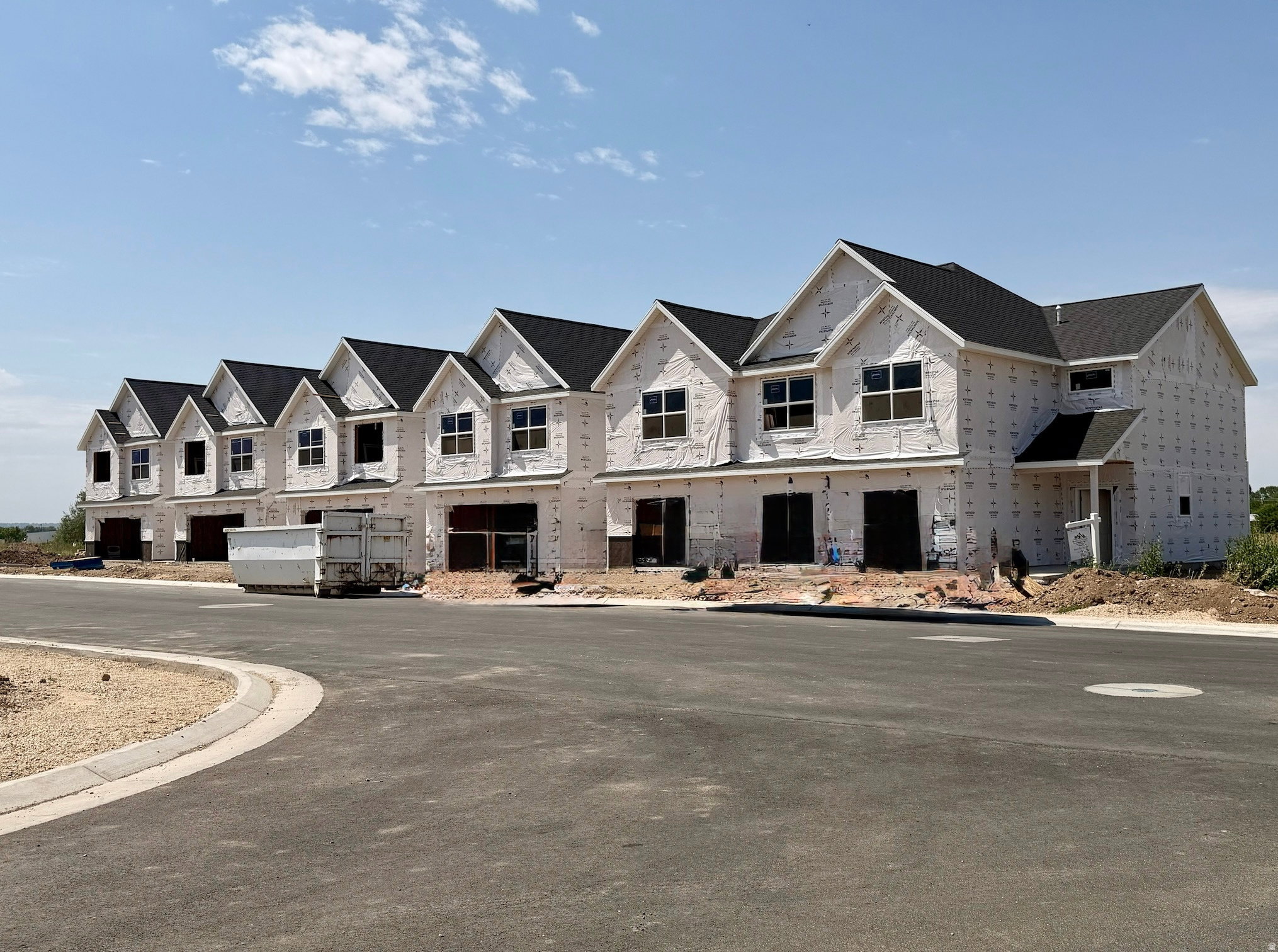 Row of newly constructed townhomes featuring dark shingle roofs, dormer windows, and attached garages