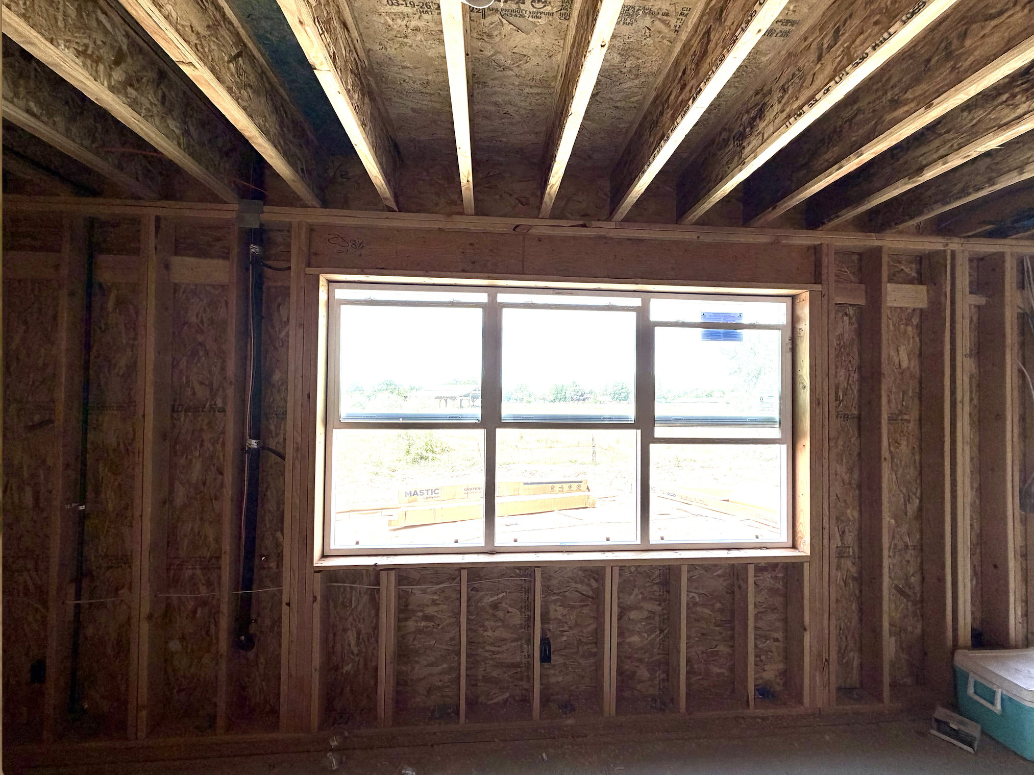 Interior framing showcasing structural wood beams, new construction window installation, and visible plumbing rough-in