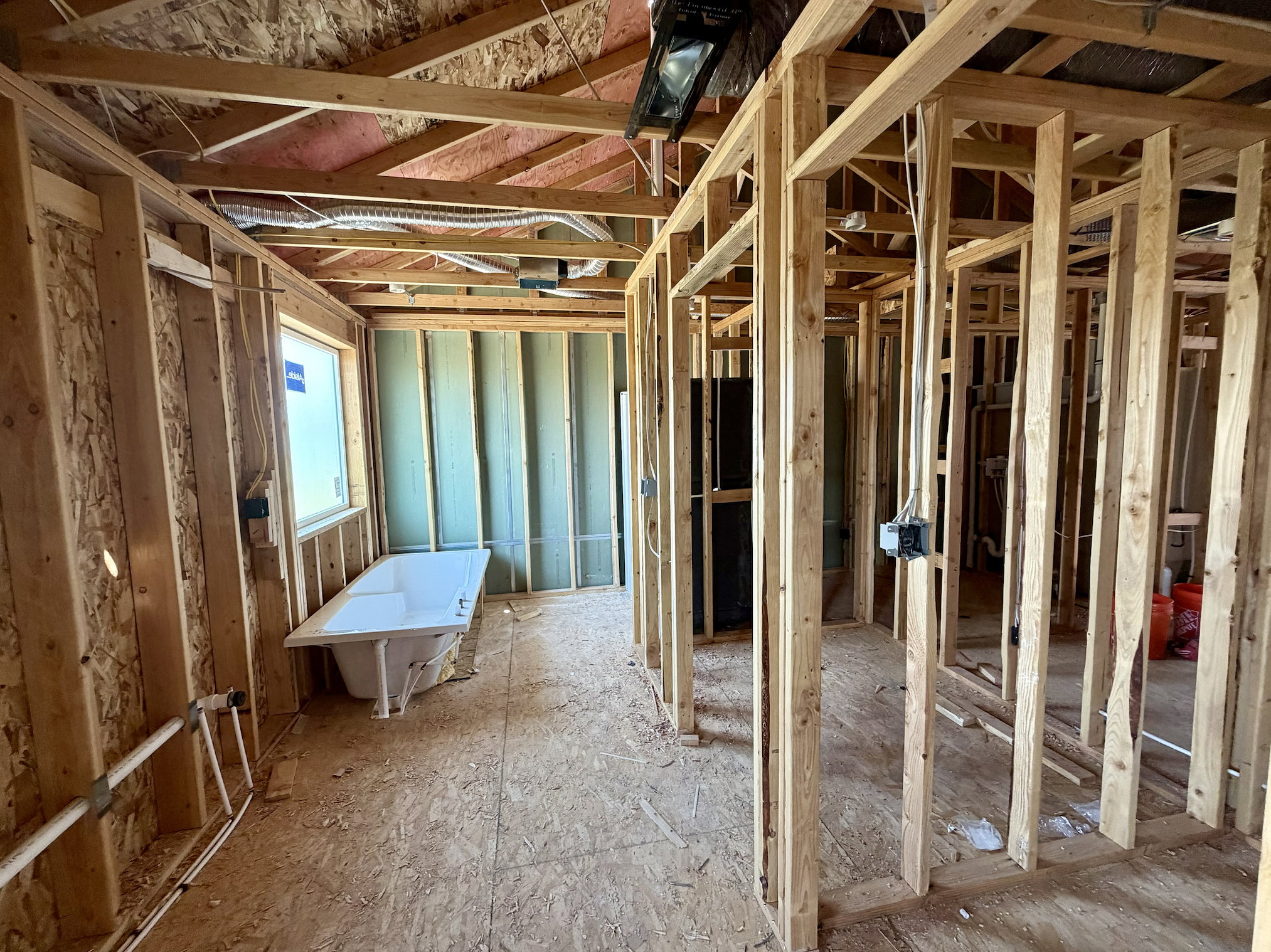 Unfinished interior space featuring wood stud framing, exposed ceiling joists, and a freestanding white bathtub