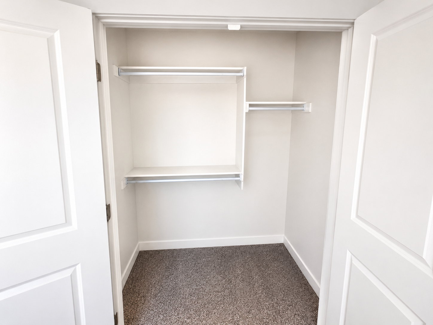 Interior closet featuring white bi-fold doors, white shelving, metal hanging rods, and carpet flooring