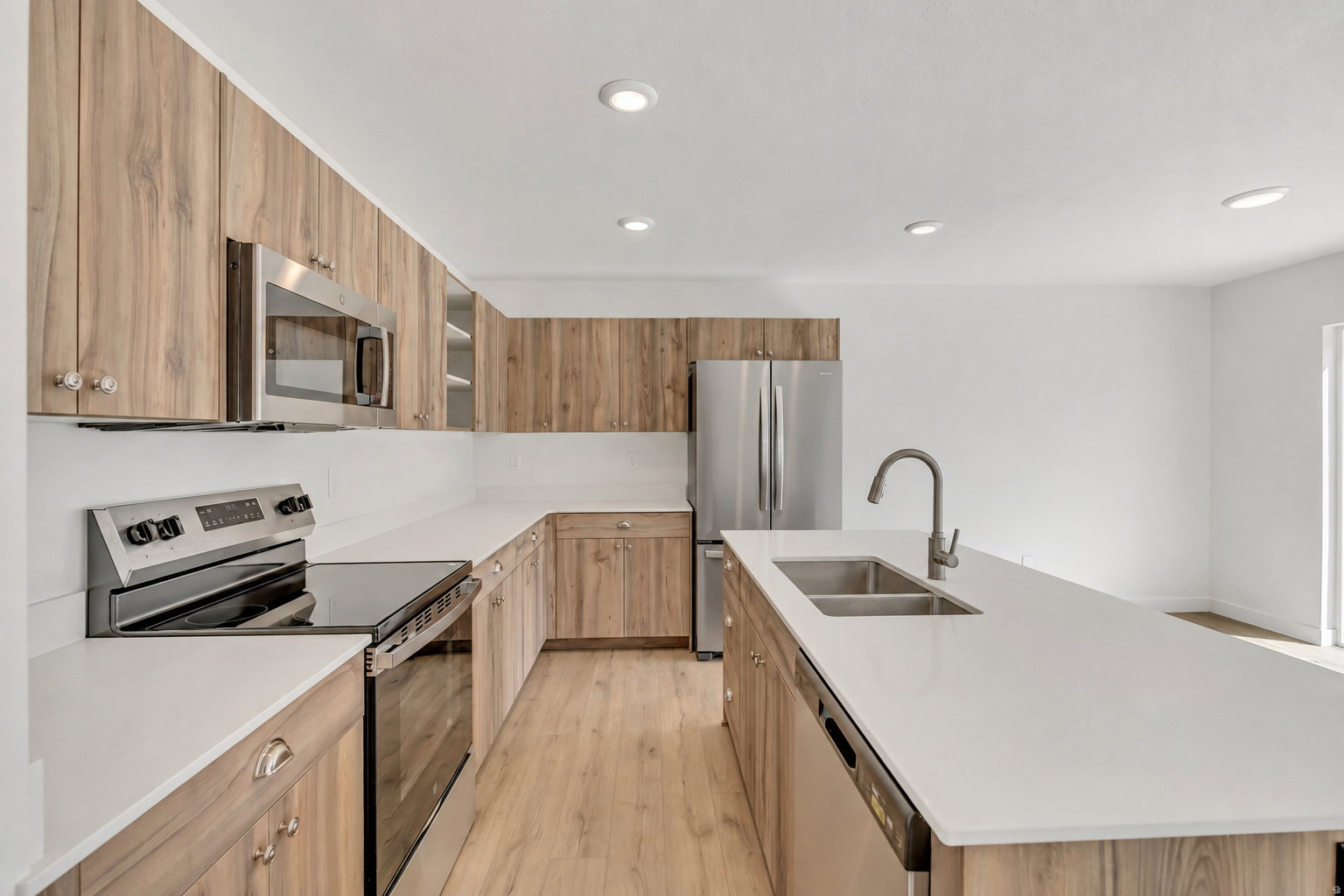 Kitchen featuring wood-finish cabinetry, stainless steel appliances, white countertops, a double basin sink, and recessed lighting