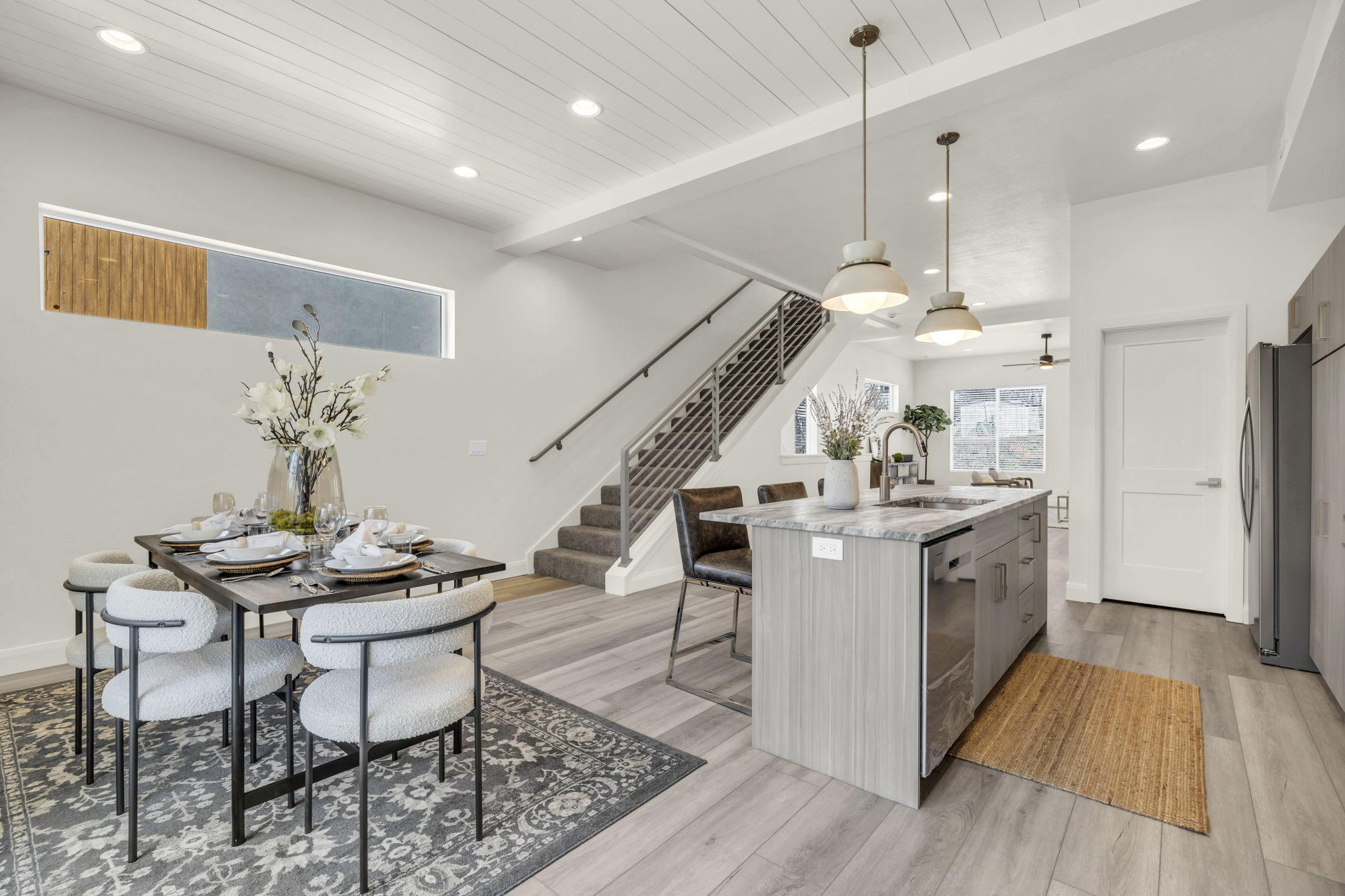Open-concept living space featuring wood-finish flooring, a contemporary staircase with metal railings, and a kitchen island with stone countertops