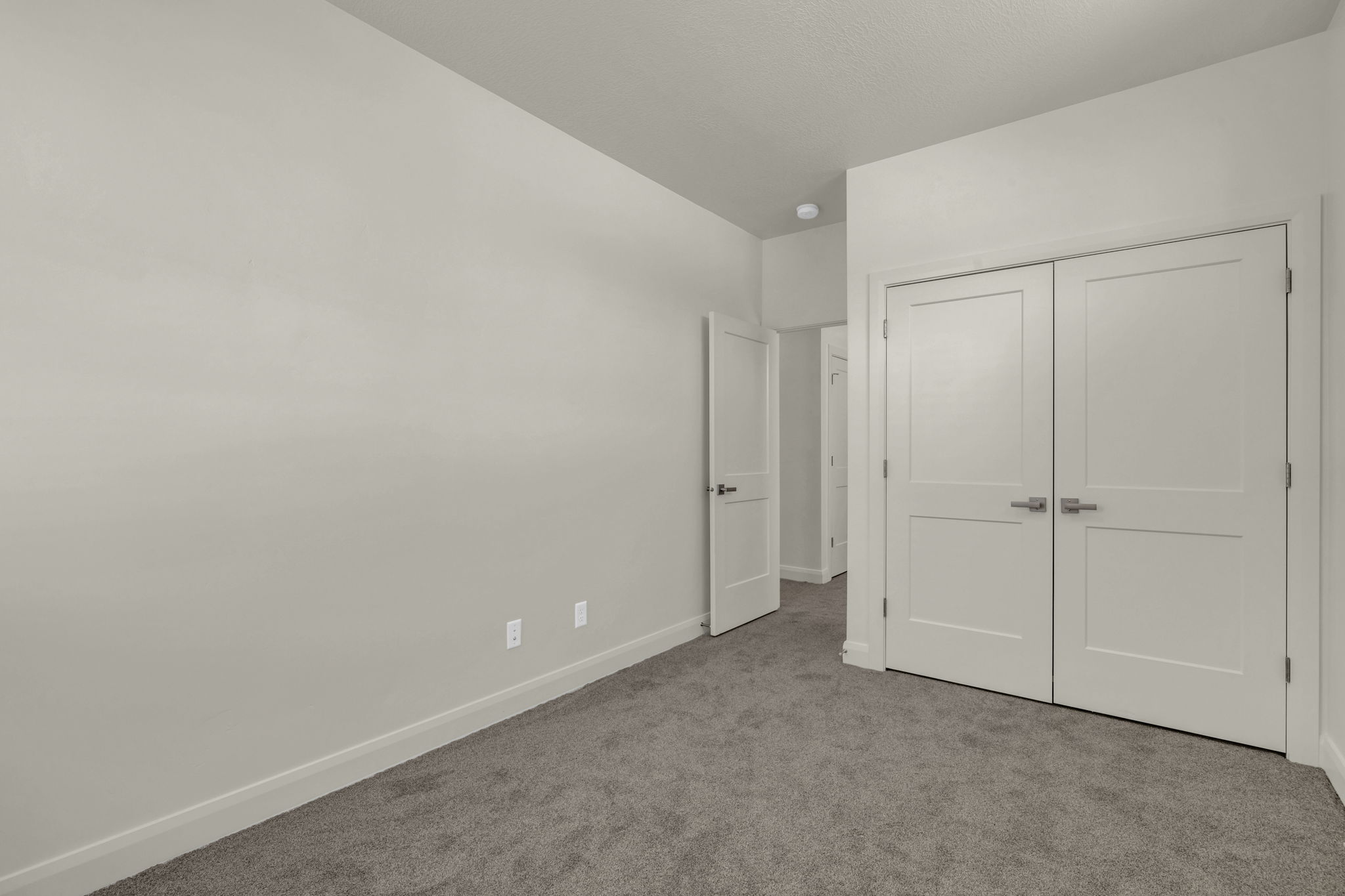 Neutral-toned interior room featuring light gray walls, dark gray carpeting, and white baseboards