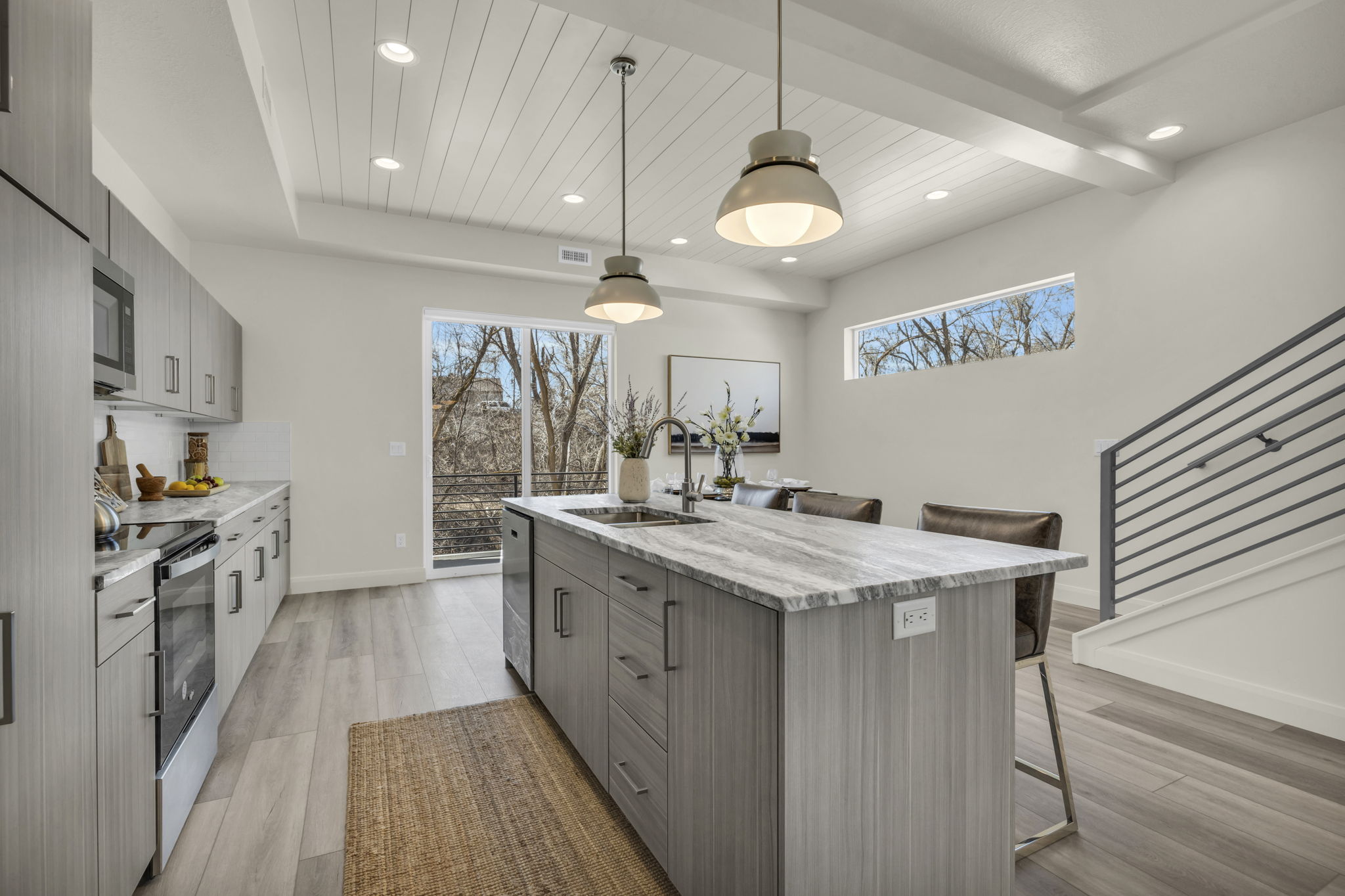 Open-concept kitchen featuring an oversized island with seating, pendant lighting, wood-finish flooring, white flat-panel cabinetry, and stainless steel appliances