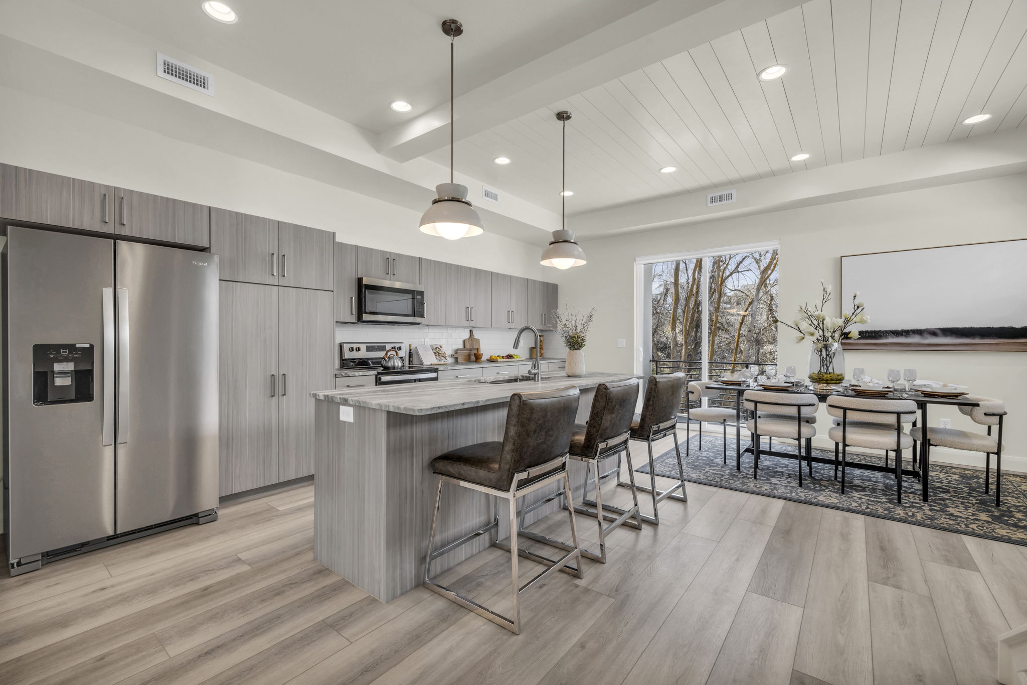 Modern kitchen featuring stainless steel appliances, grey wood-finish cabinetry, light stone-finish countertops, and an island with pendant lighting