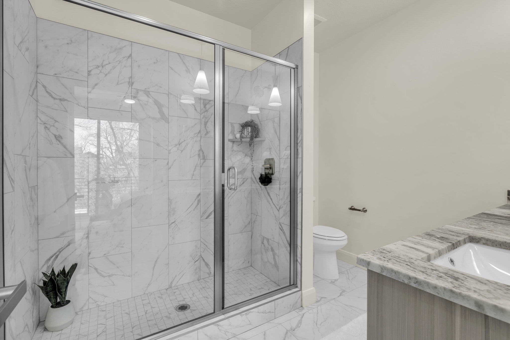Glass-enclosed shower with white marble-look tile, dual pendant lights, and a built-in shower niche