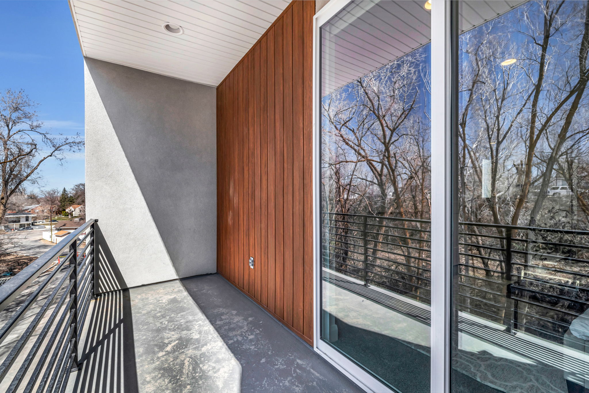 Private balcony featuring a black metal railing, concrete flooring, wood-finish wall paneling, and stucco siding