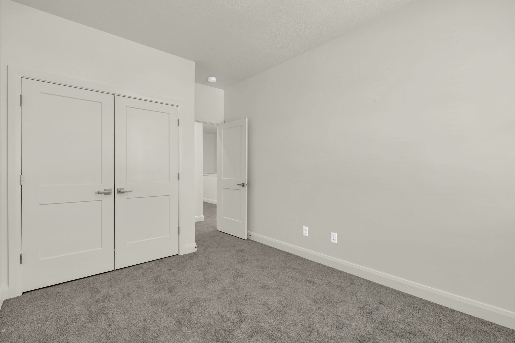 Room featuring neutral-toned carpeting, light-colored walls, and a pair of white panel doors with brushed nickel hardware