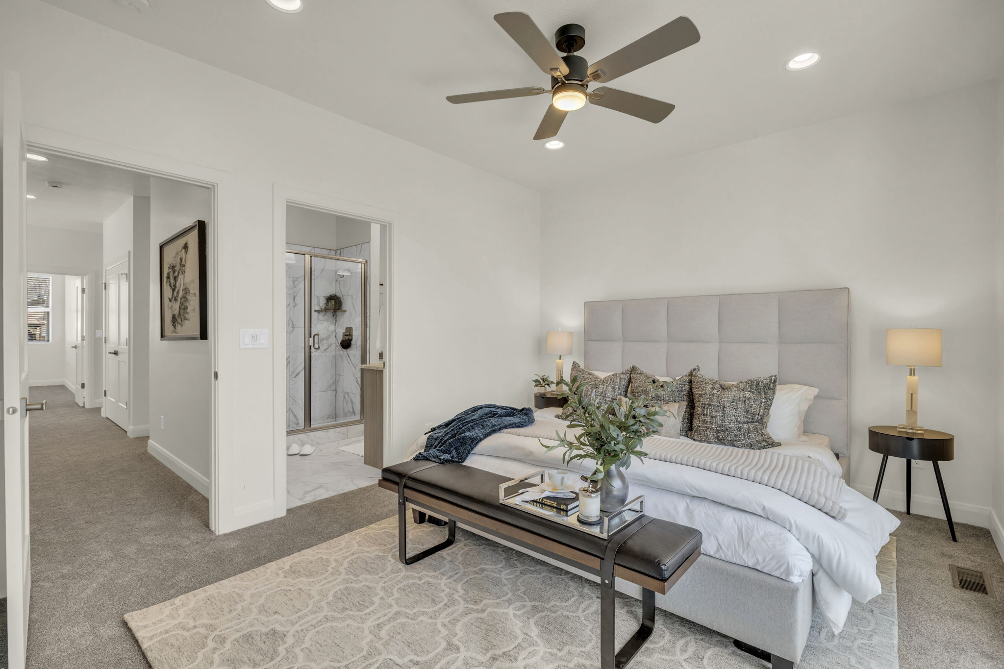 Bright bedroom featuring recessed lighting, a ceiling fan, plush carpet flooring, and an open doorway to a bathroom with a glass-enclosed shower
