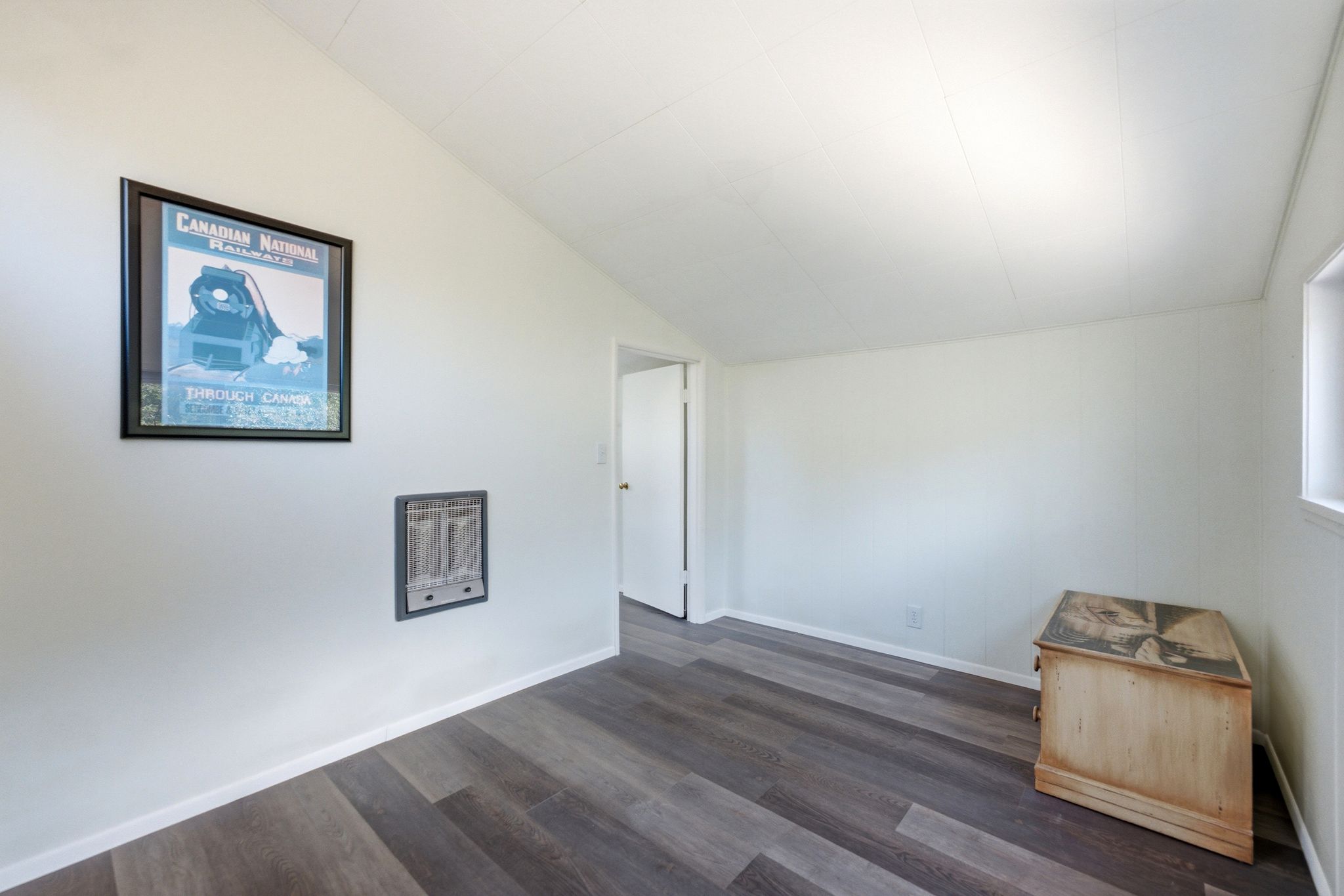 Room featuring wood-finish flooring, a wall-mounted heating unit, and a white interior door frame