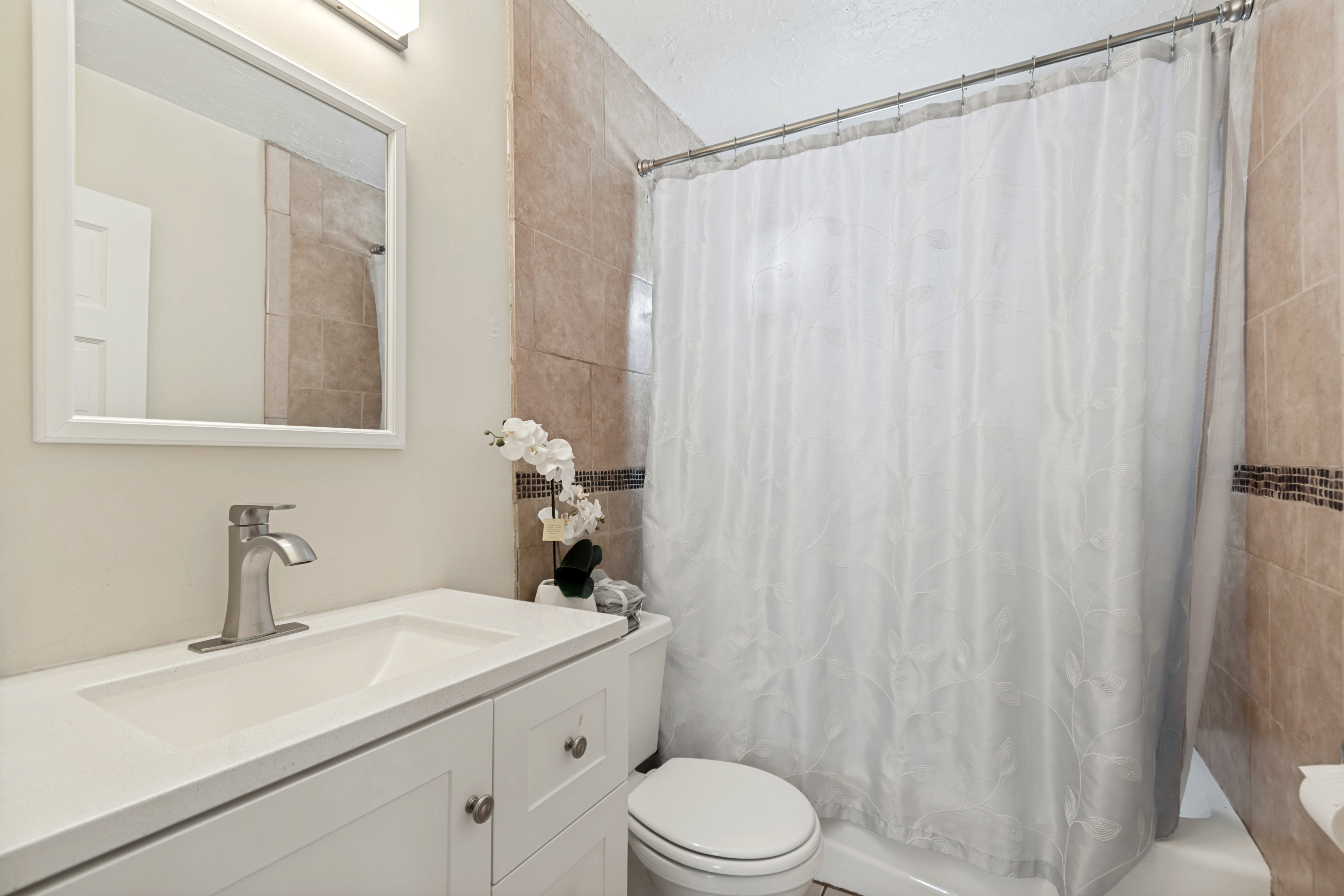 Bathroom featuring a white vanity with integrated sink, brushed nickel faucet, framed mirror, and tiled shower surround with decorative accent band