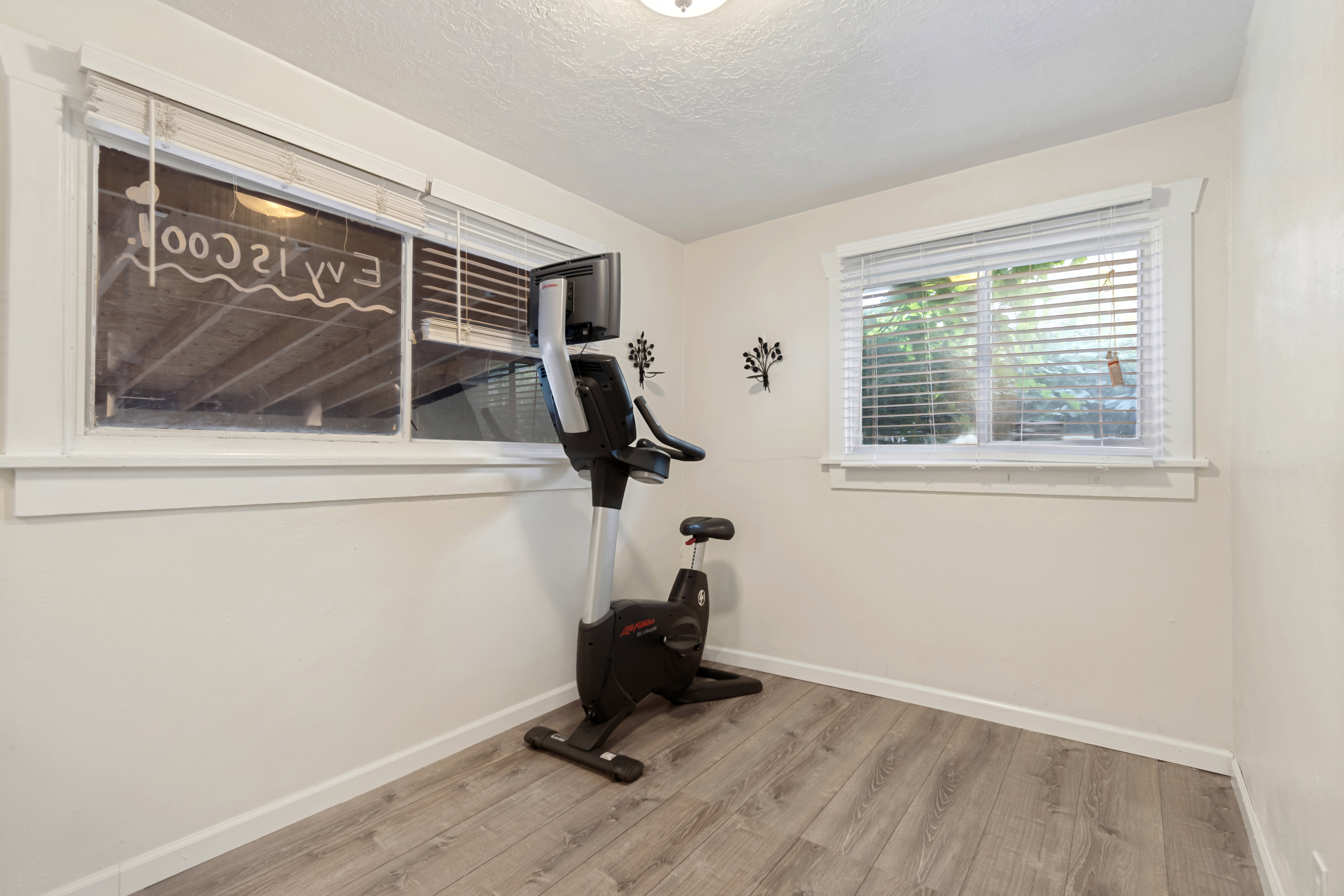 Versatile room featuring two windows with white blinds, neutral wall paint, and wood-finish flooring