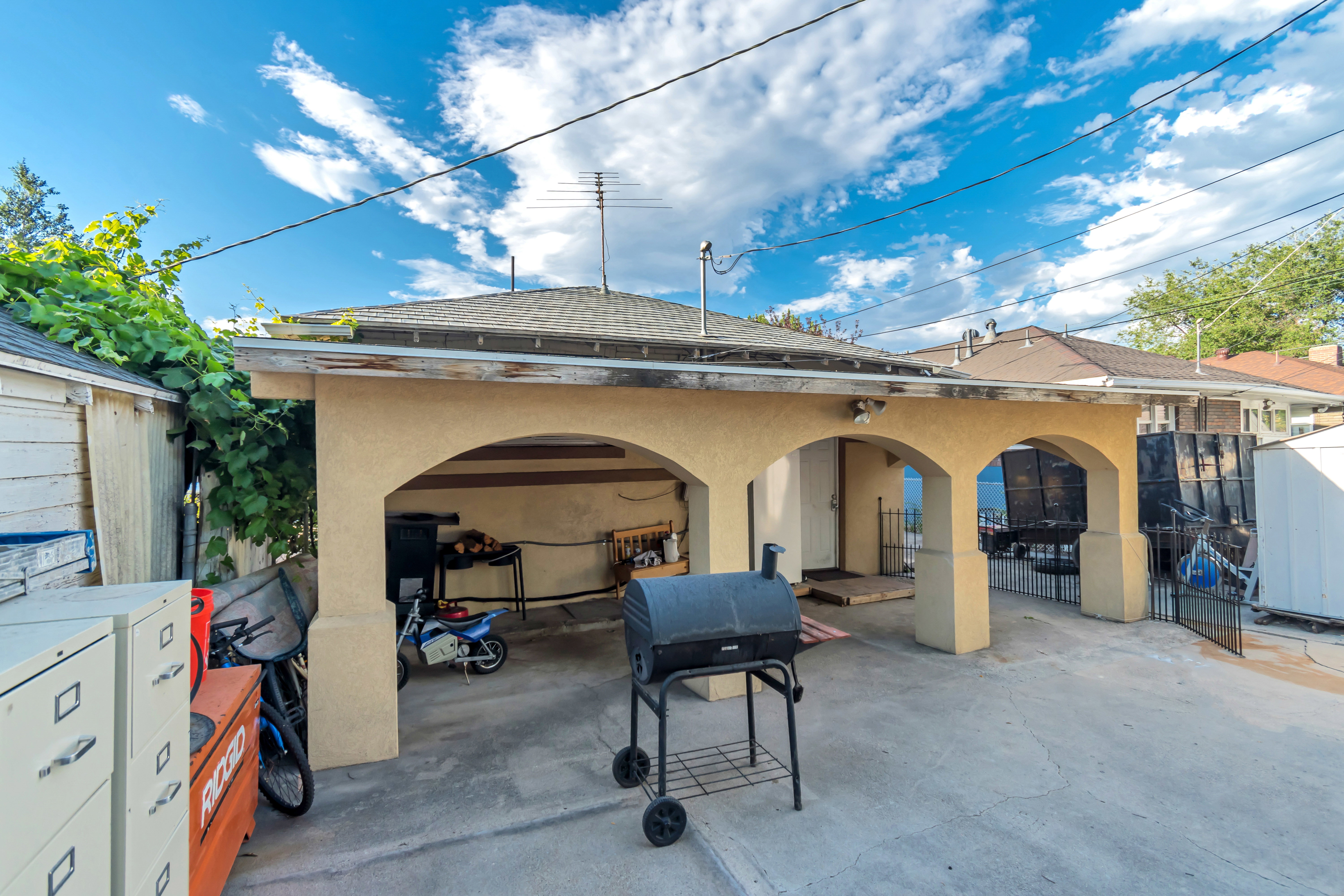 Rear exterior featuring a multi-arched carport structure, a concrete driveway, a shingled roof, and a privacy fence