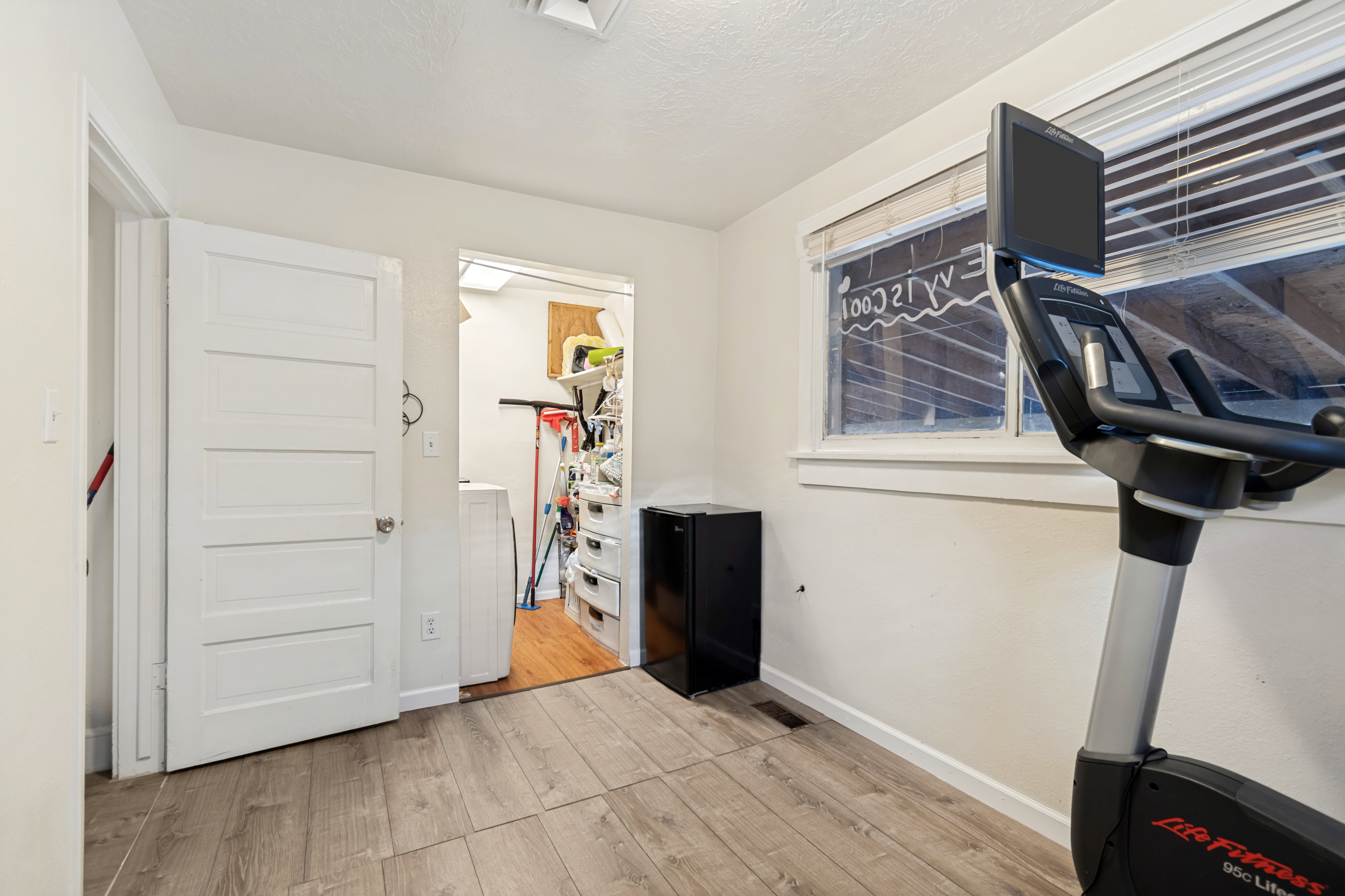 Room featuring wood-finish flooring, white walls, and a window with horizontal blinds