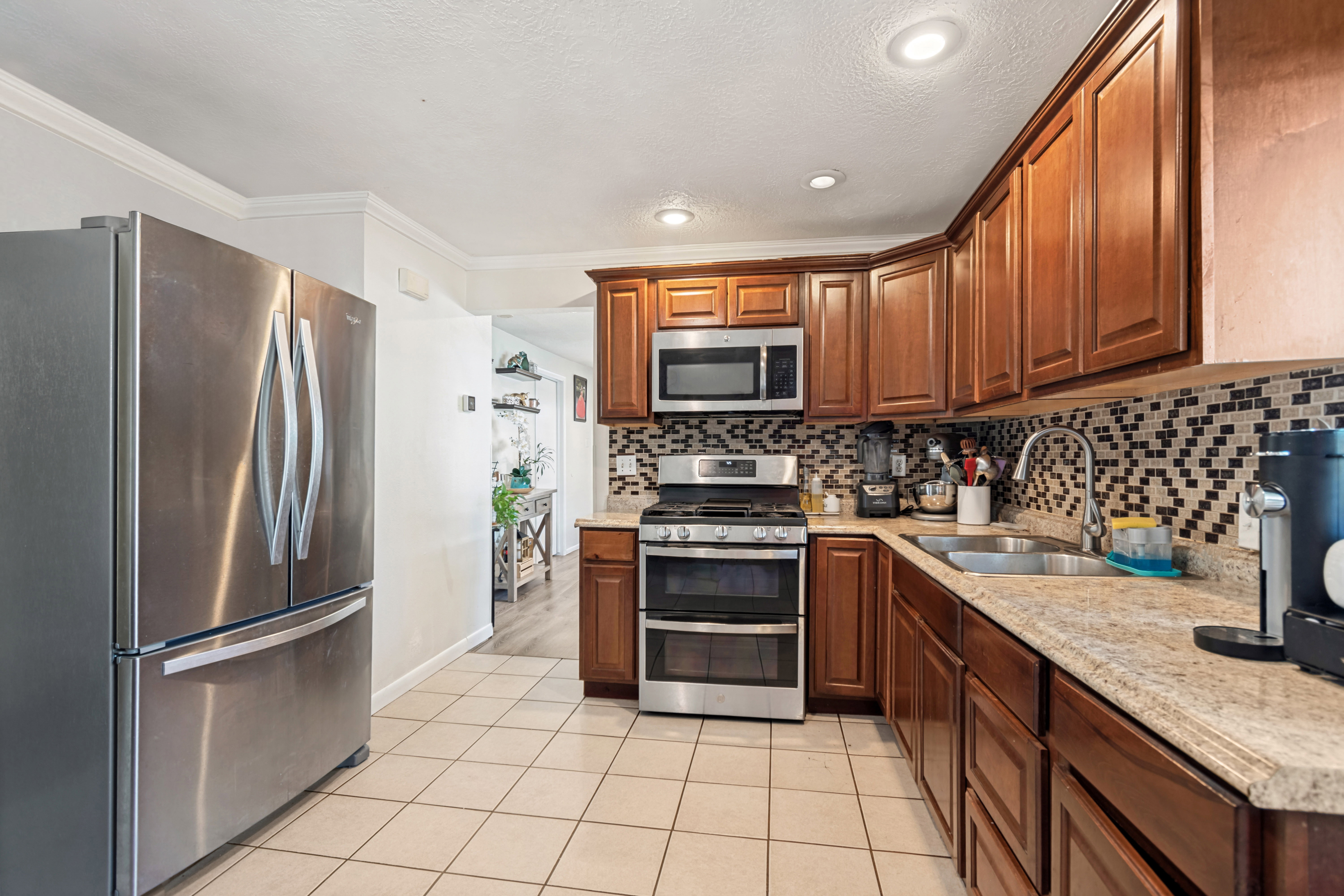 Kitchen featuring warm wood-finish cabinetry, light speckled countertops, a patterned tile backsplash, and light tile flooring