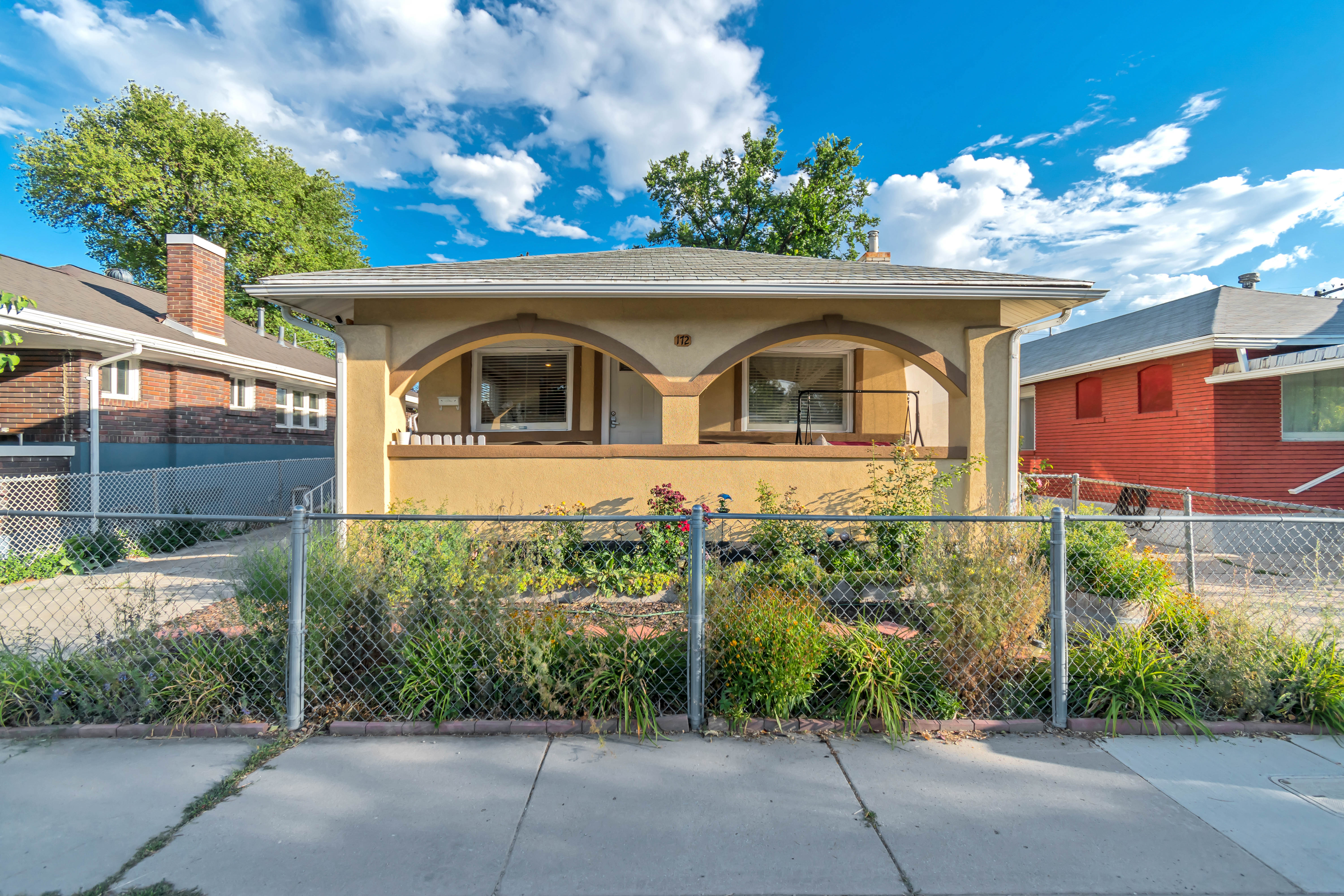 Exterior facade featuring a covered porch with arched openings, stucco finish, and a chain-link fence
