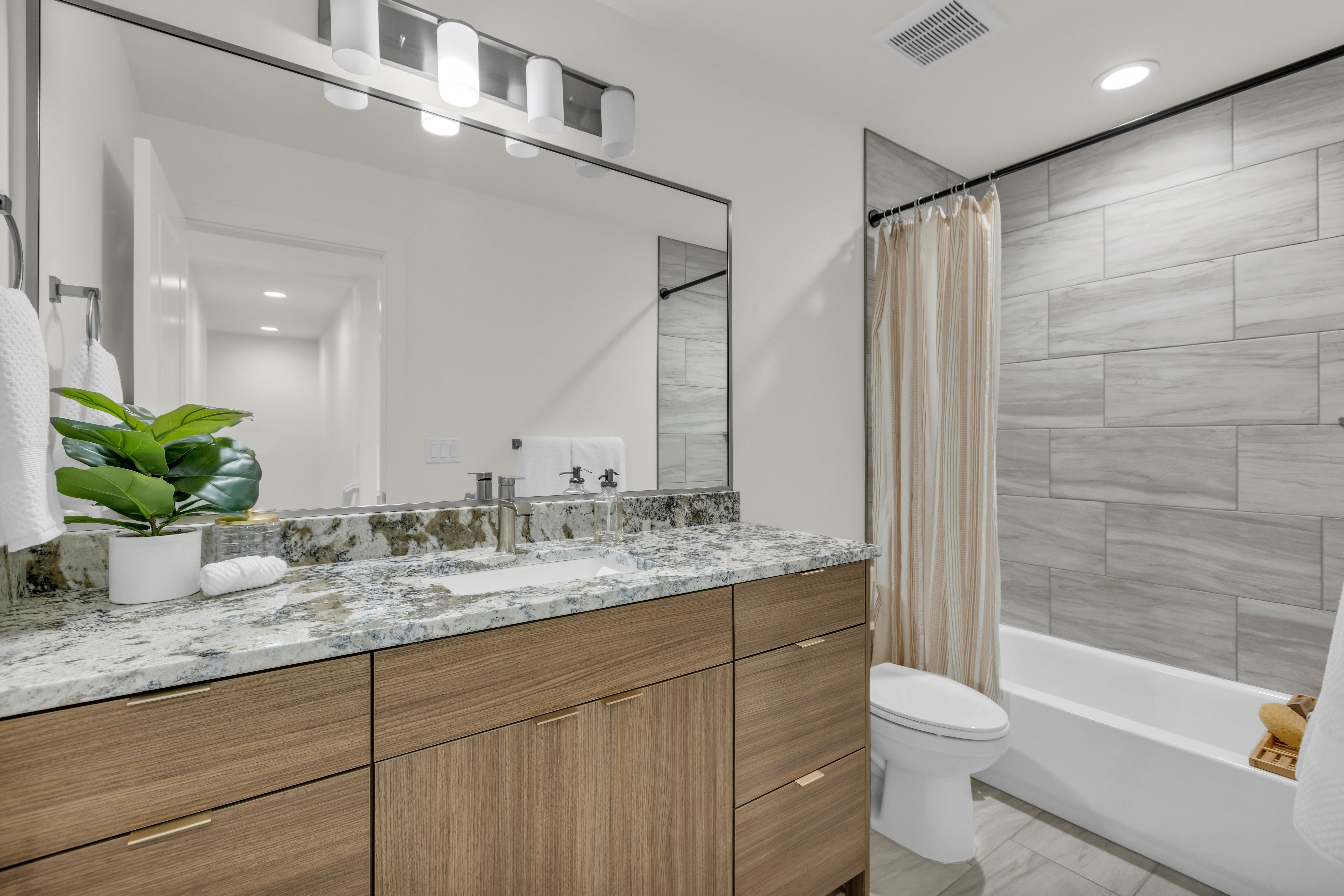 Bathroom featuring a large vanity with a patterned countertop, wood-finish cabinetry, a single undermount sink, and a framed mirror