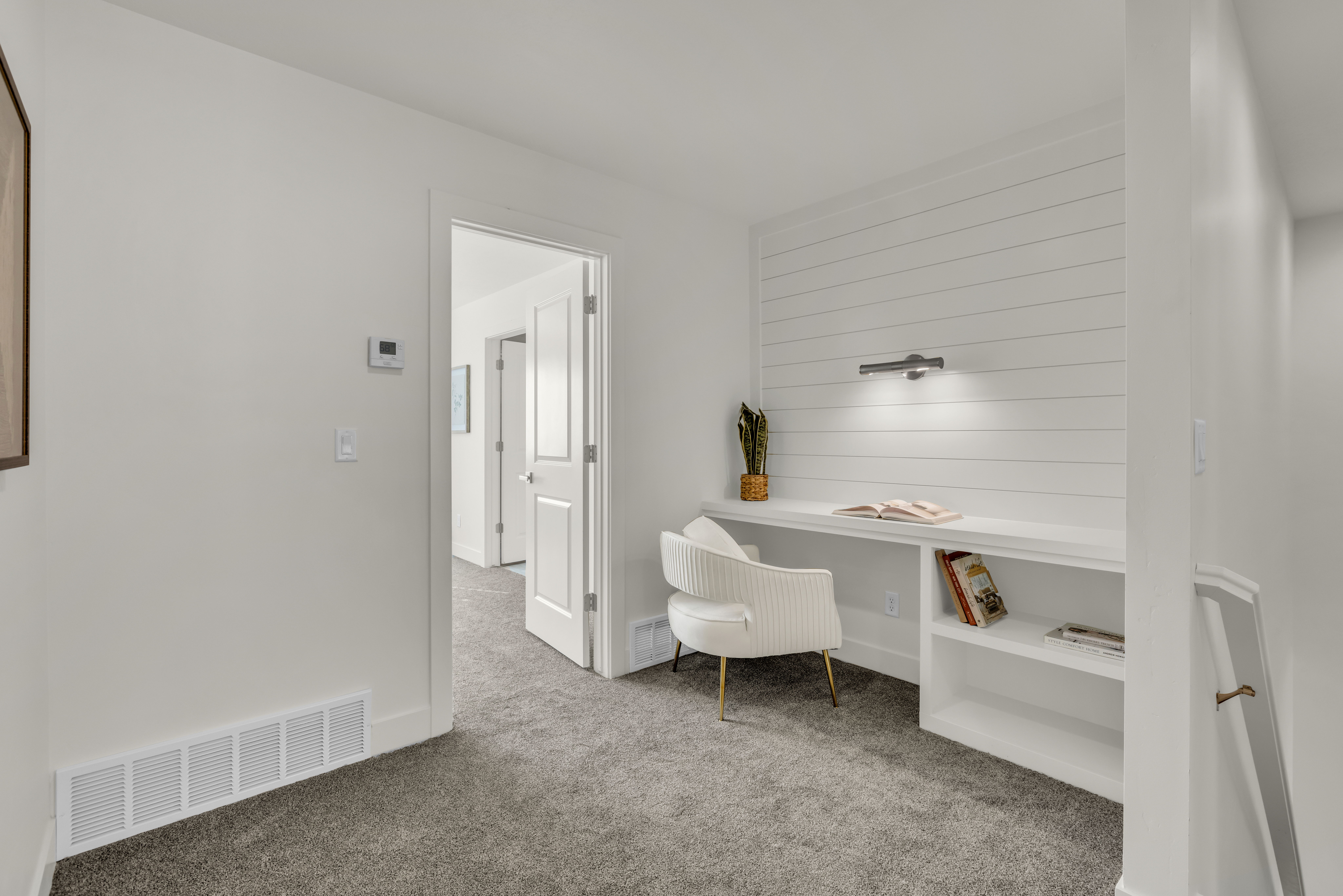 Integrated desk space featuring a shiplap accent wall with an attached task light, built-in shelving, and neutral carpet flooring