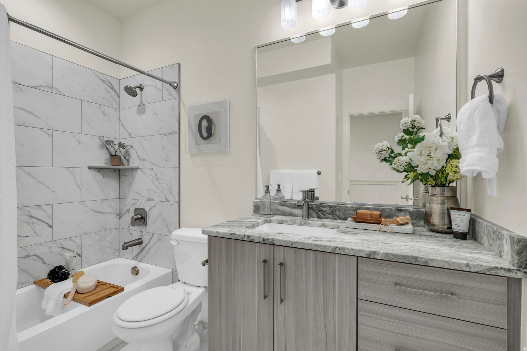 Full bathroom featuring a white tub with marble-look tile surround, a built-in corner shelf, and brushed nickel fixtures