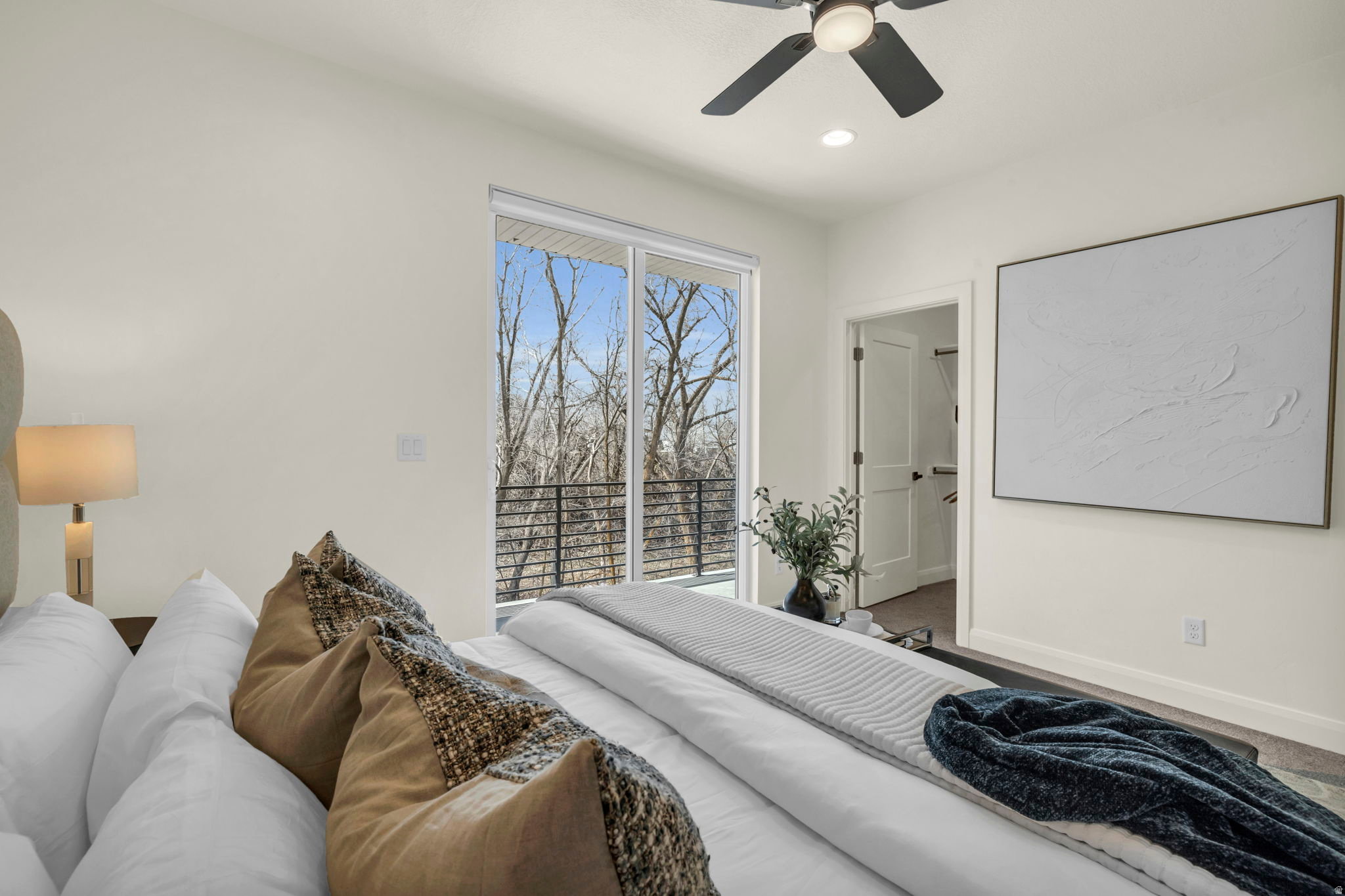 Spacious room featuring floor-to-ceiling sliding glass doors, a private balcony with black metal railings, a ceiling fan with integrated lighting, recessed lighting, and a white paneled door leading to a closet