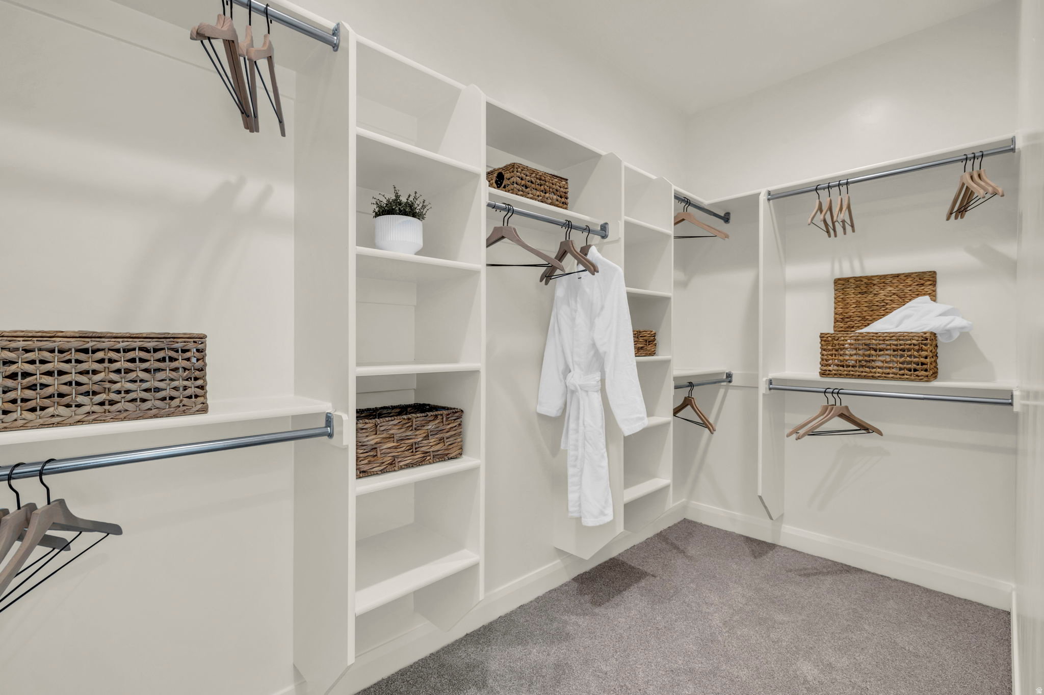 Walk-in closet featuring built-in shelving, multiple hanging rods, white cabinetry, neutral wall color, and grey carpet flooring