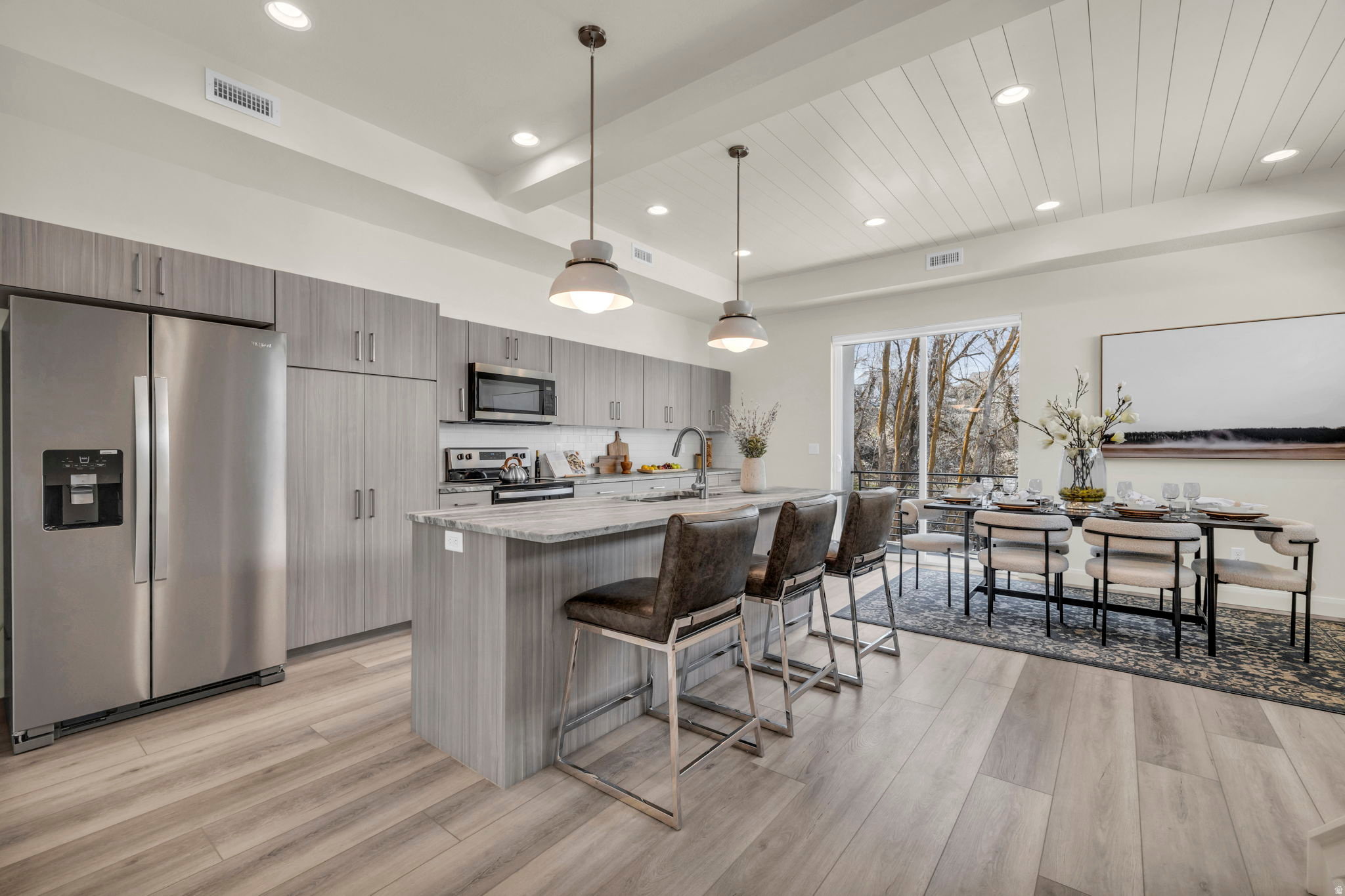 Open-concept kitchen and dining area featuring light wood-finish flooring, a kitchen island with seating, stainless steel appliances, modern cabinetry, and a shiplap ceiling