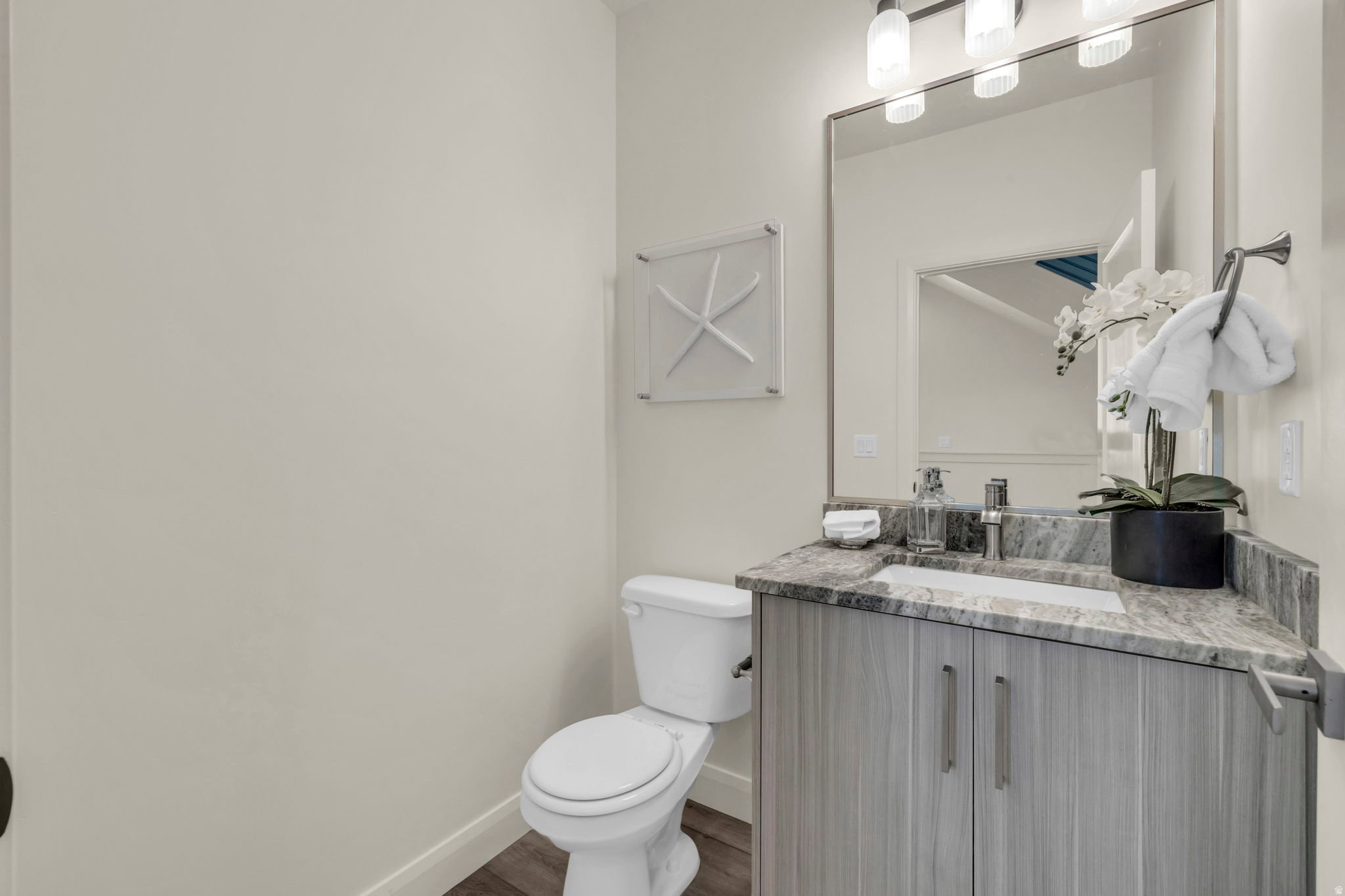 Bathroom featuring wood-finish flooring, a contemporary vanity with a stone countertop, an undermount sink, and a framed mirror with overhead lighting