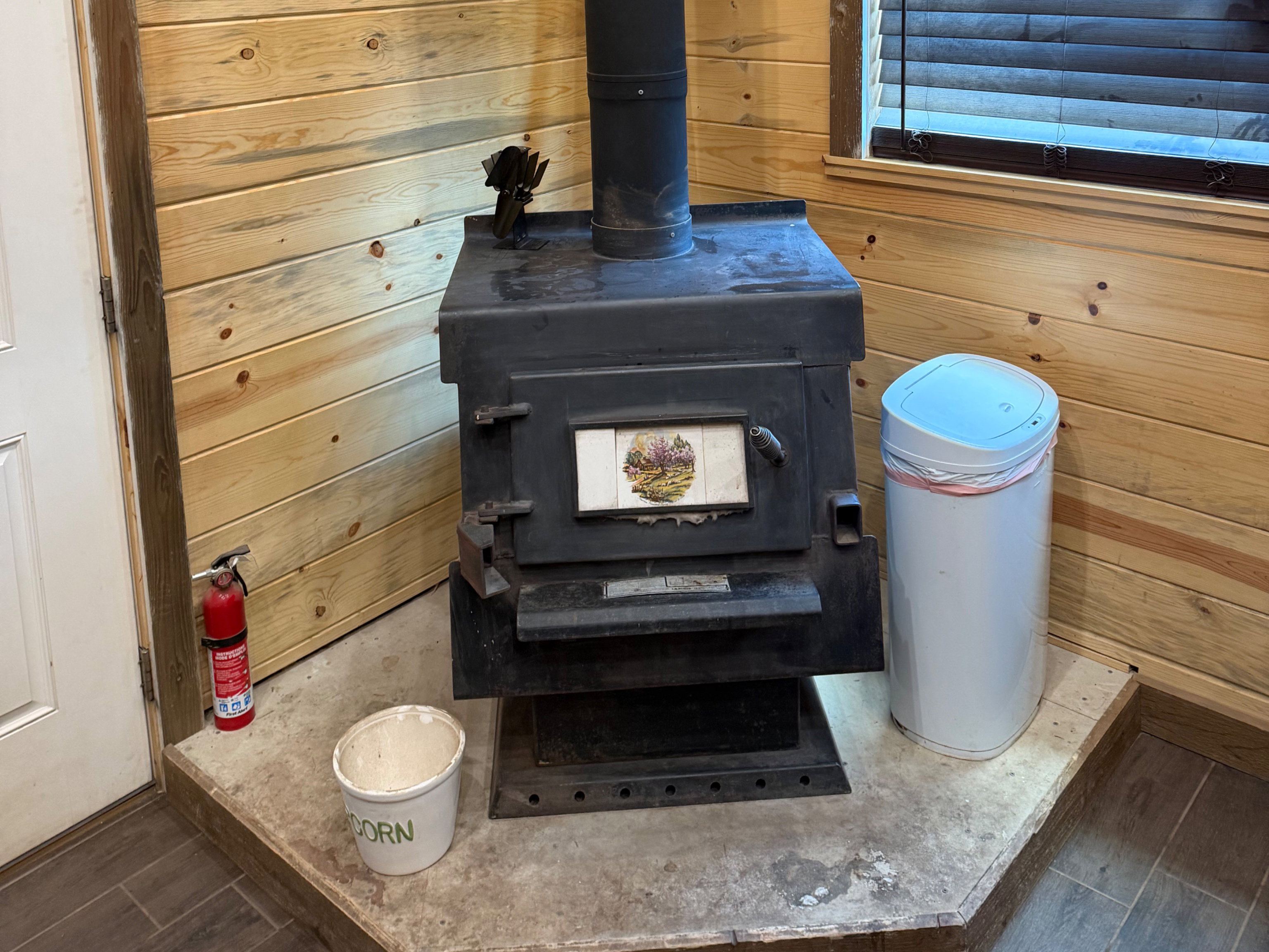 Black wood-burning stove with a metal flue pipe, set on a raised hearth with tile flooring