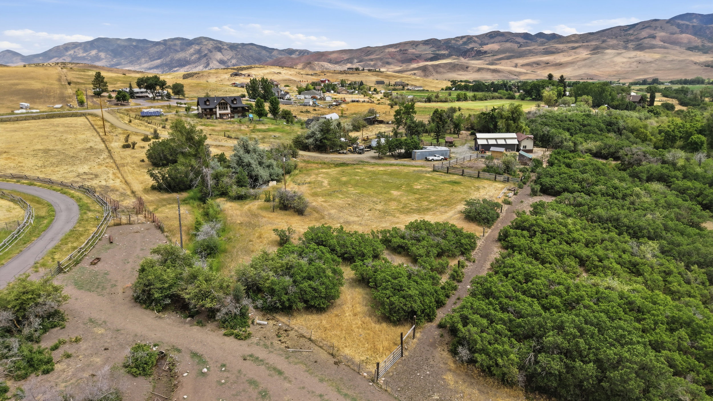 Expansive rural landscape featuring a winding paved road, diverse vegetation, and distant mountain ranges