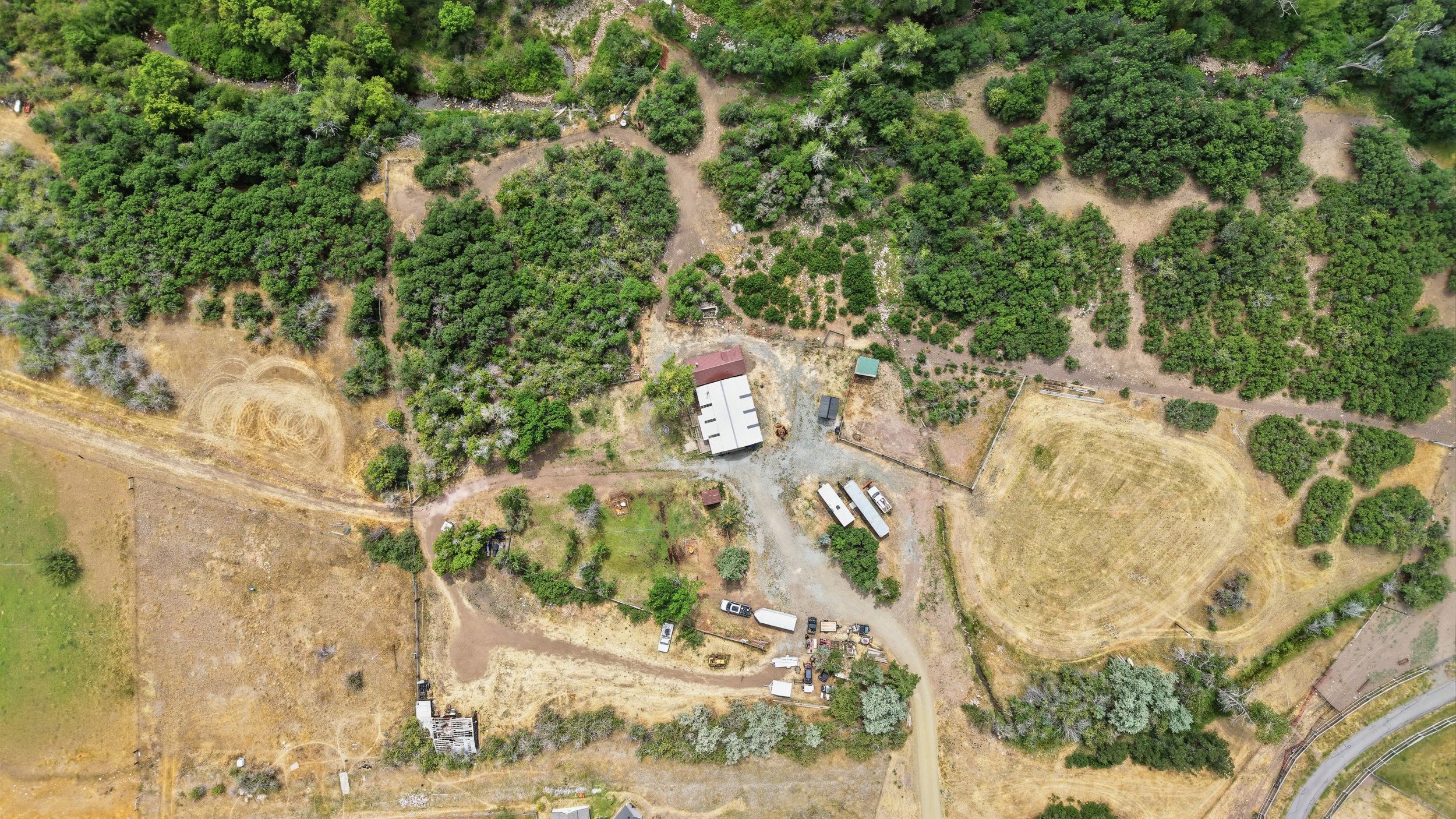 Expansive property featuring a central building, multiple outbuildings, and varied terrain including wooded areas and open fields