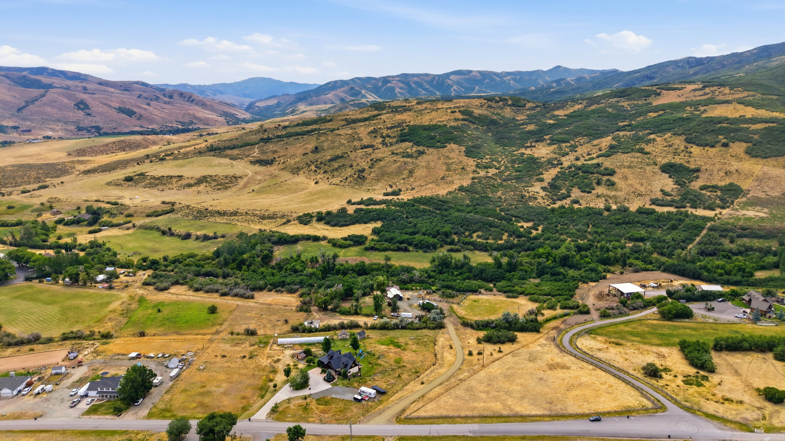Expansive rural property featuring a winding paved road, a cluster of buildings with white roofs, and a separate large residence with a black roof