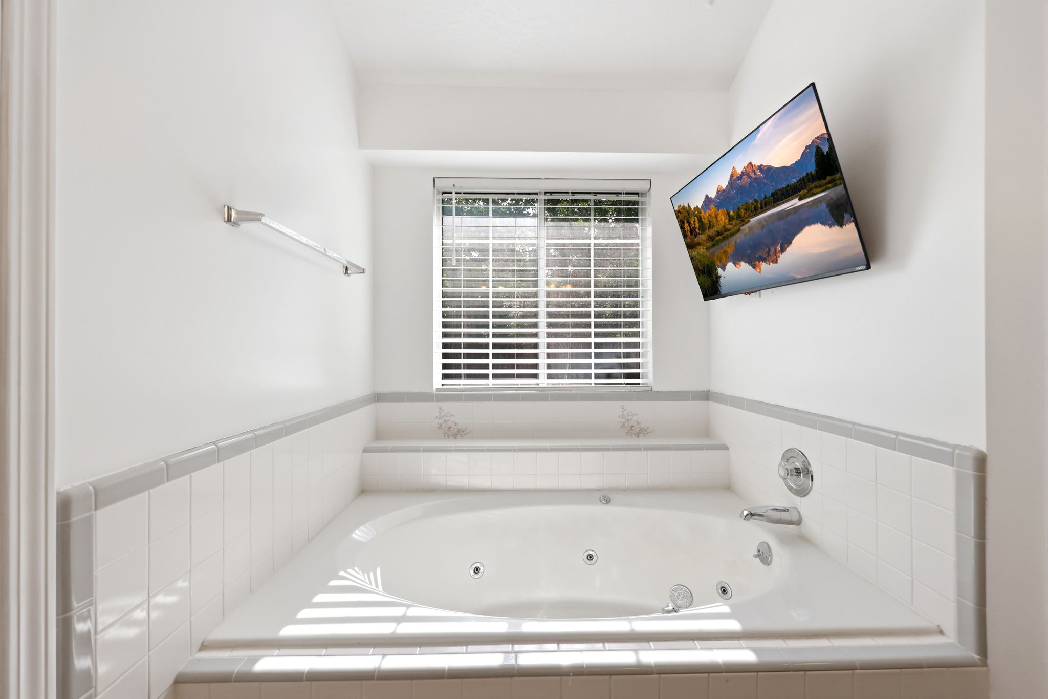 Soaking tub with jets, white tile surround, privacy blinds, and chrome fixtures