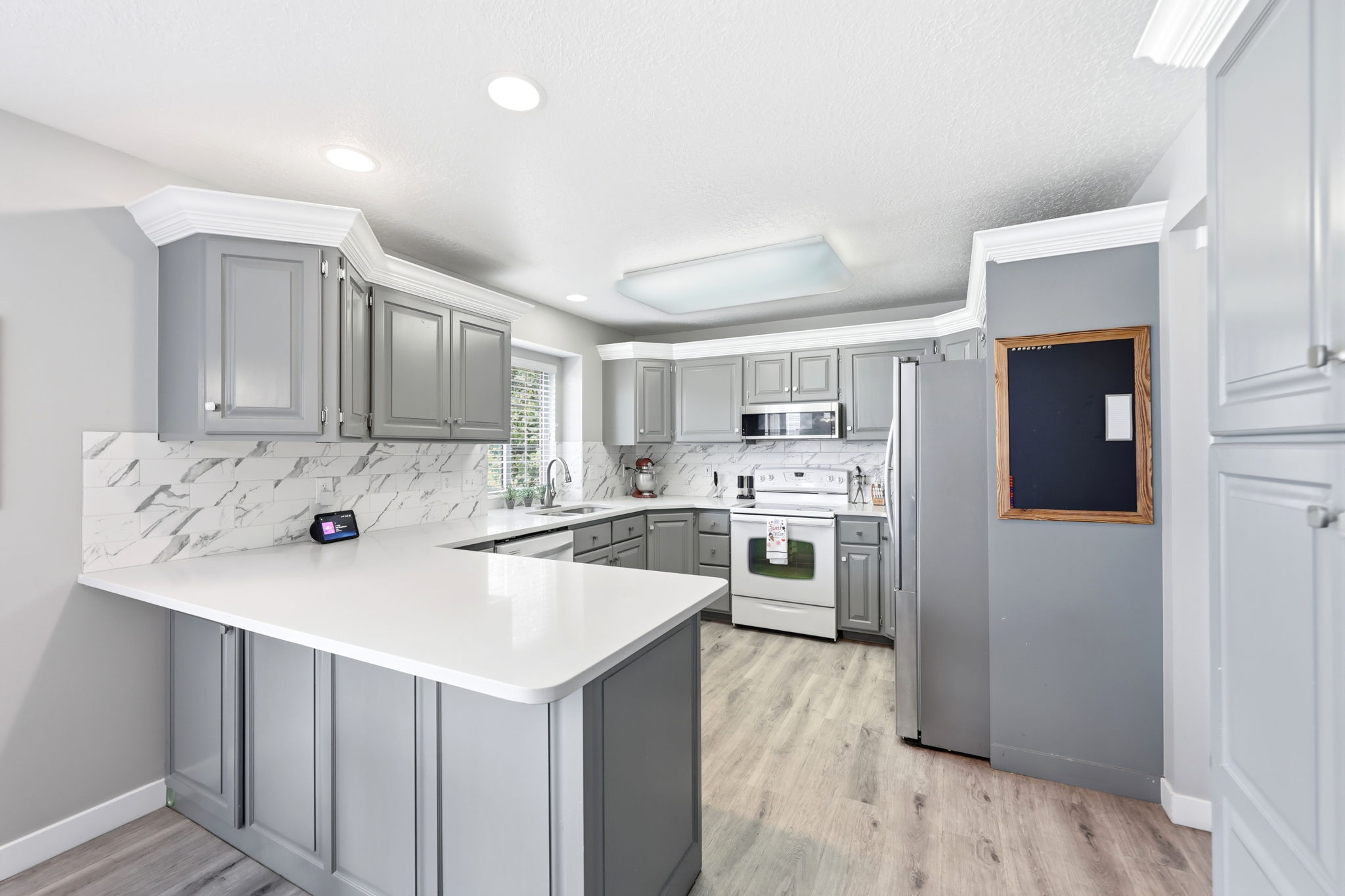 Kitchen featuring gray cabinetry, white countertops, marble-look tile backsplash, stainless steel appliances, and wood-finish flooring