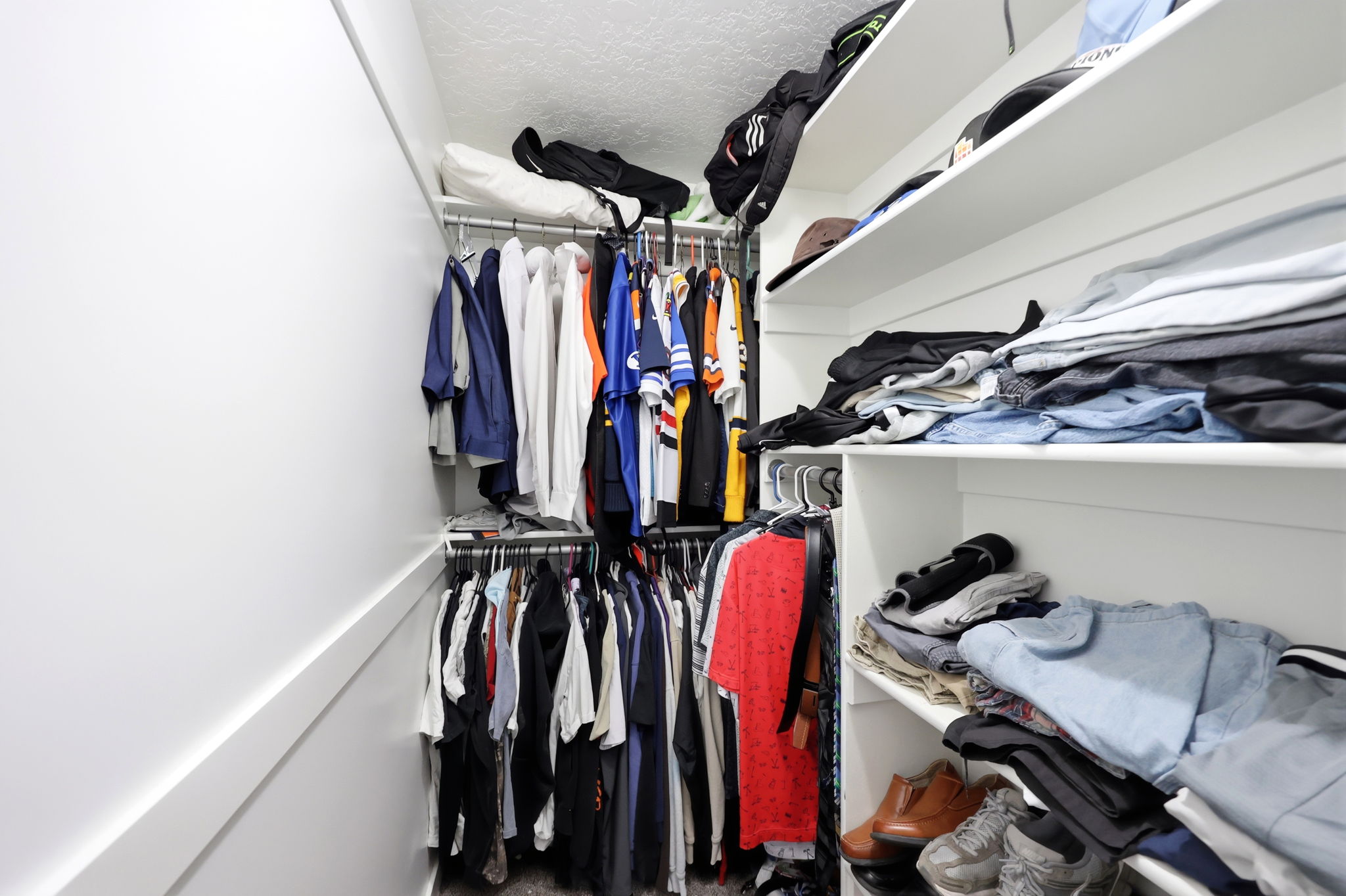 Walk-in closet featuring built-in shelving, multiple hanging rods, white walls, and a textured ceiling