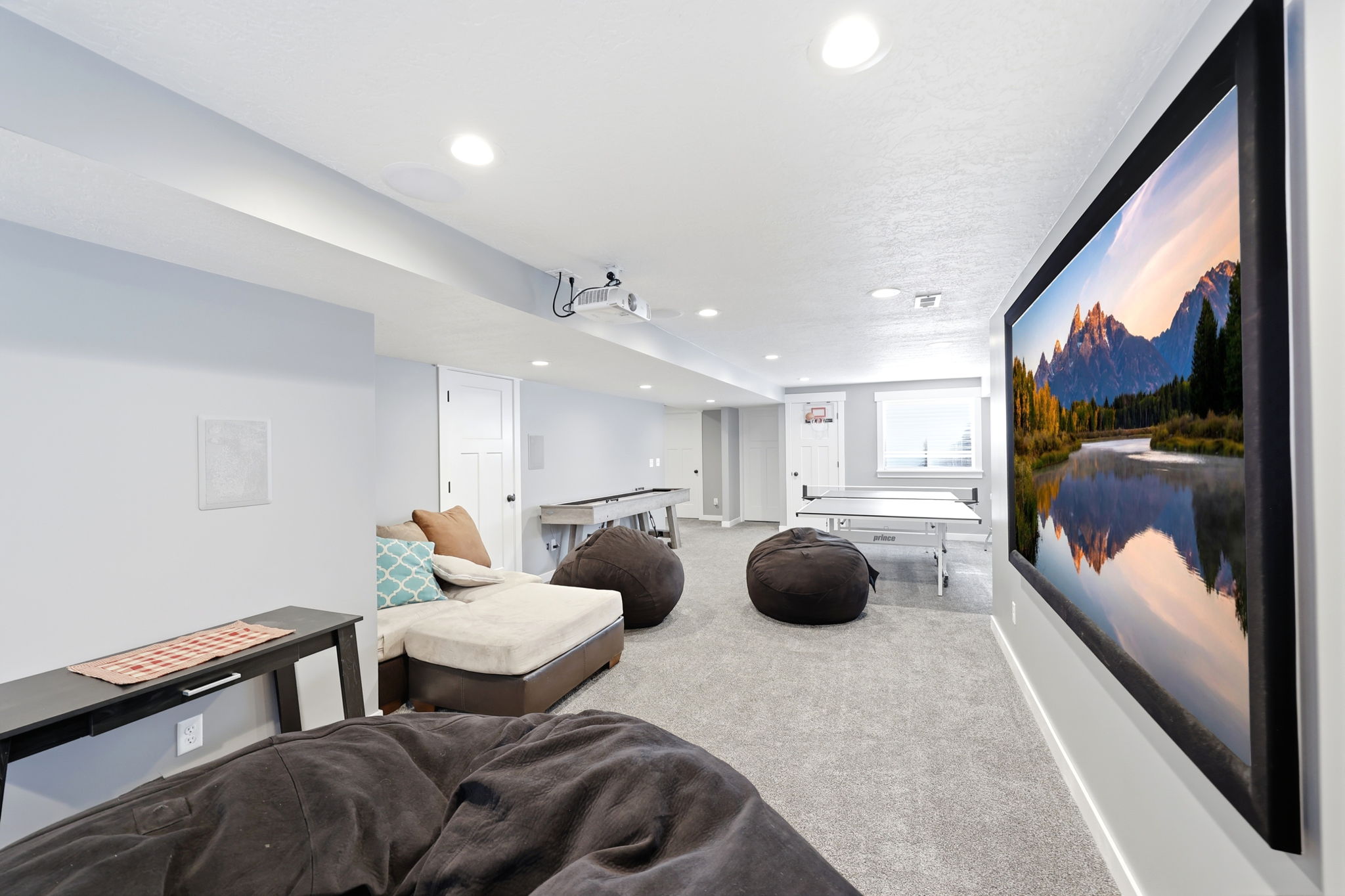 Expansive recreation room featuring a large wall-mounted screen, recessed lighting, and light gray carpeting