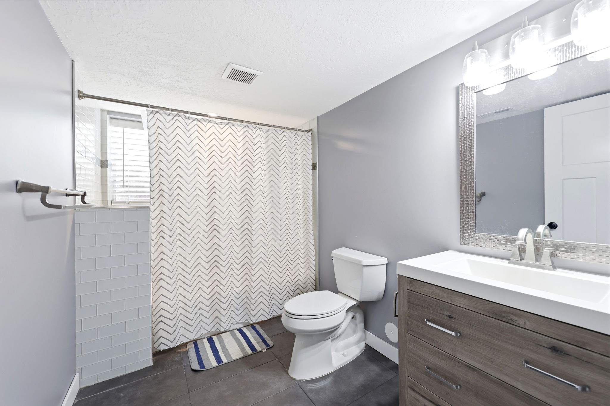 Modern bathroom featuring a contemporary vanity with a white countertop and integrated sink, a textured framed mirror, and a wall-mounted light fixture