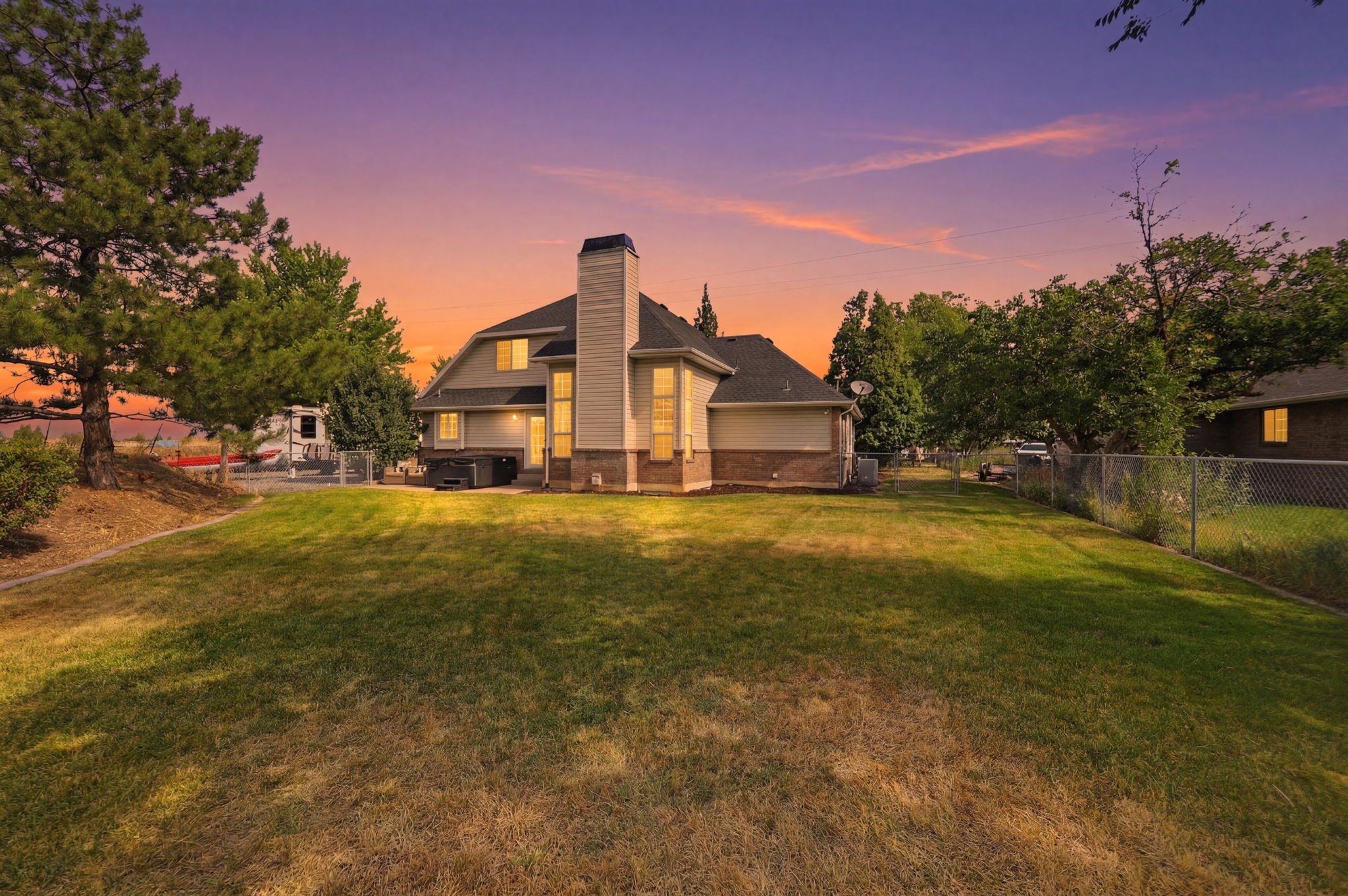 Expansive grassy yard with mature trees and a chain-link fence