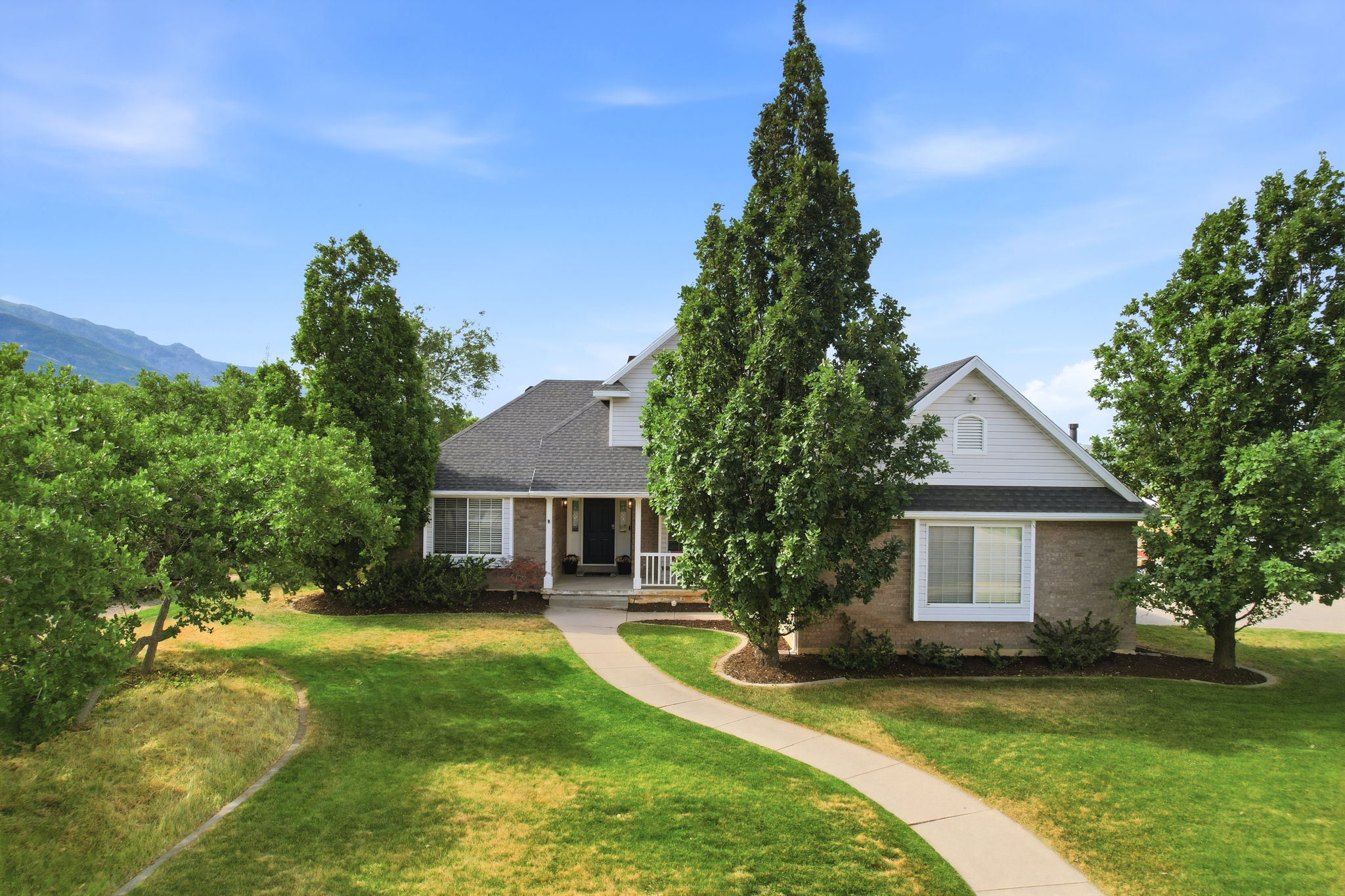 Traditional-style residence featuring a brick and siding exterior, a prominent front porch with white railings, and a dark shingle roof