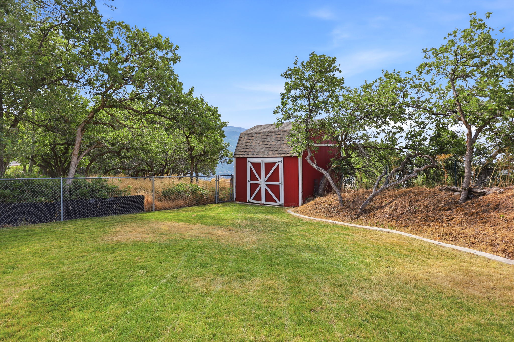 Expansive green lawn with a red storage shed featuring white trim and a shingled roof