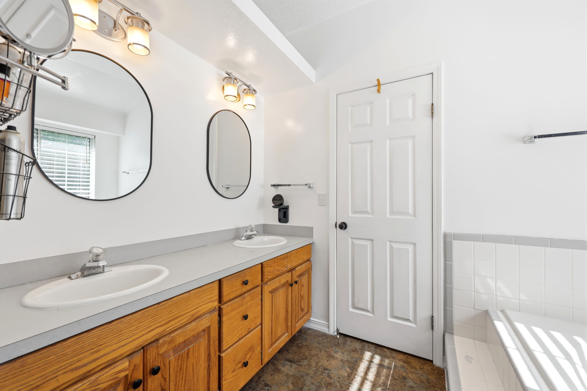 Double vanity featuring wood cabinetry with black hardware, two oval mirrors, and overhead light fixtures