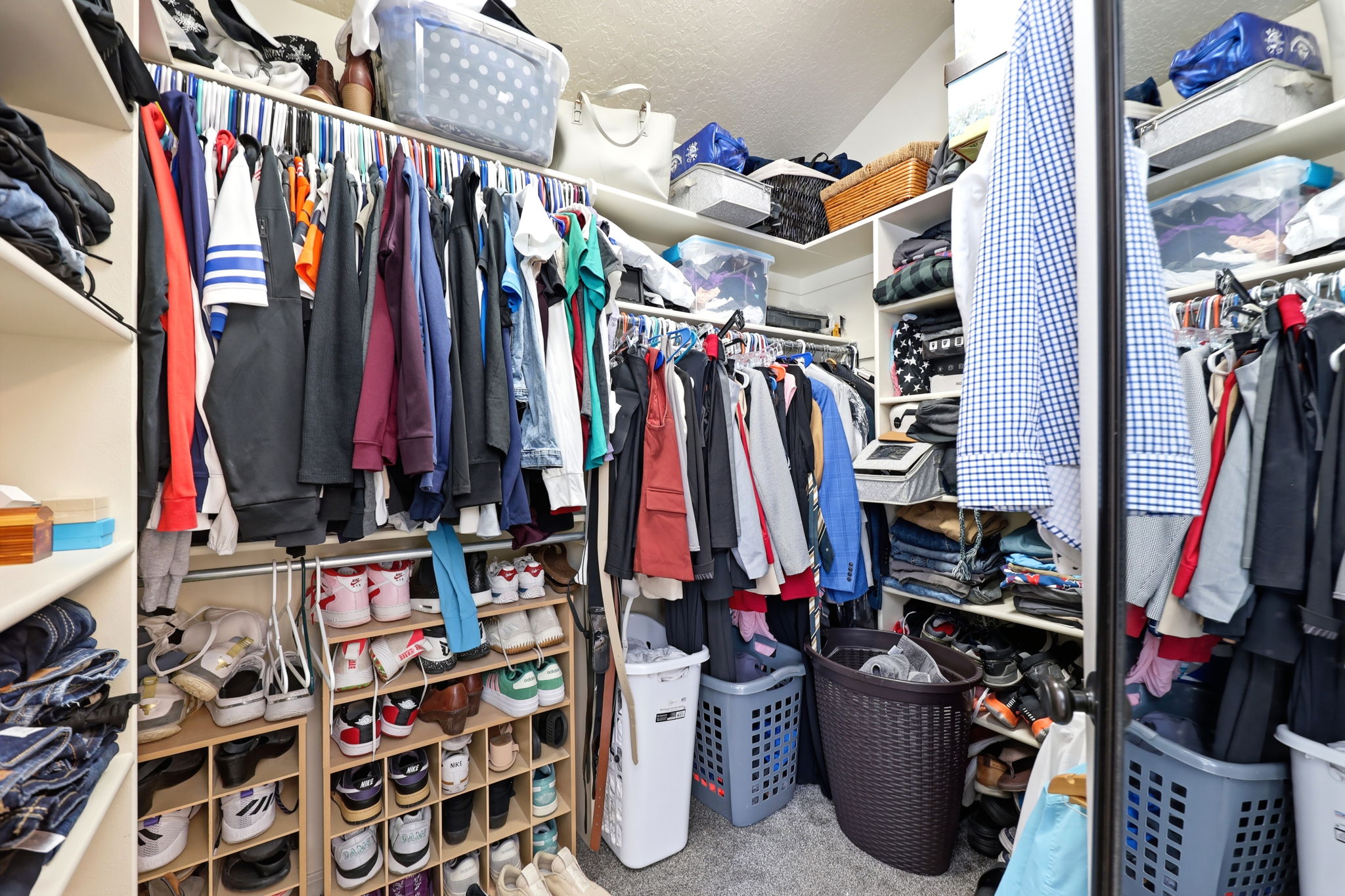 Walk-in closet featuring extensive built-in shelving, multiple hanging rods, dedicated shoe storage, and soft carpet flooring