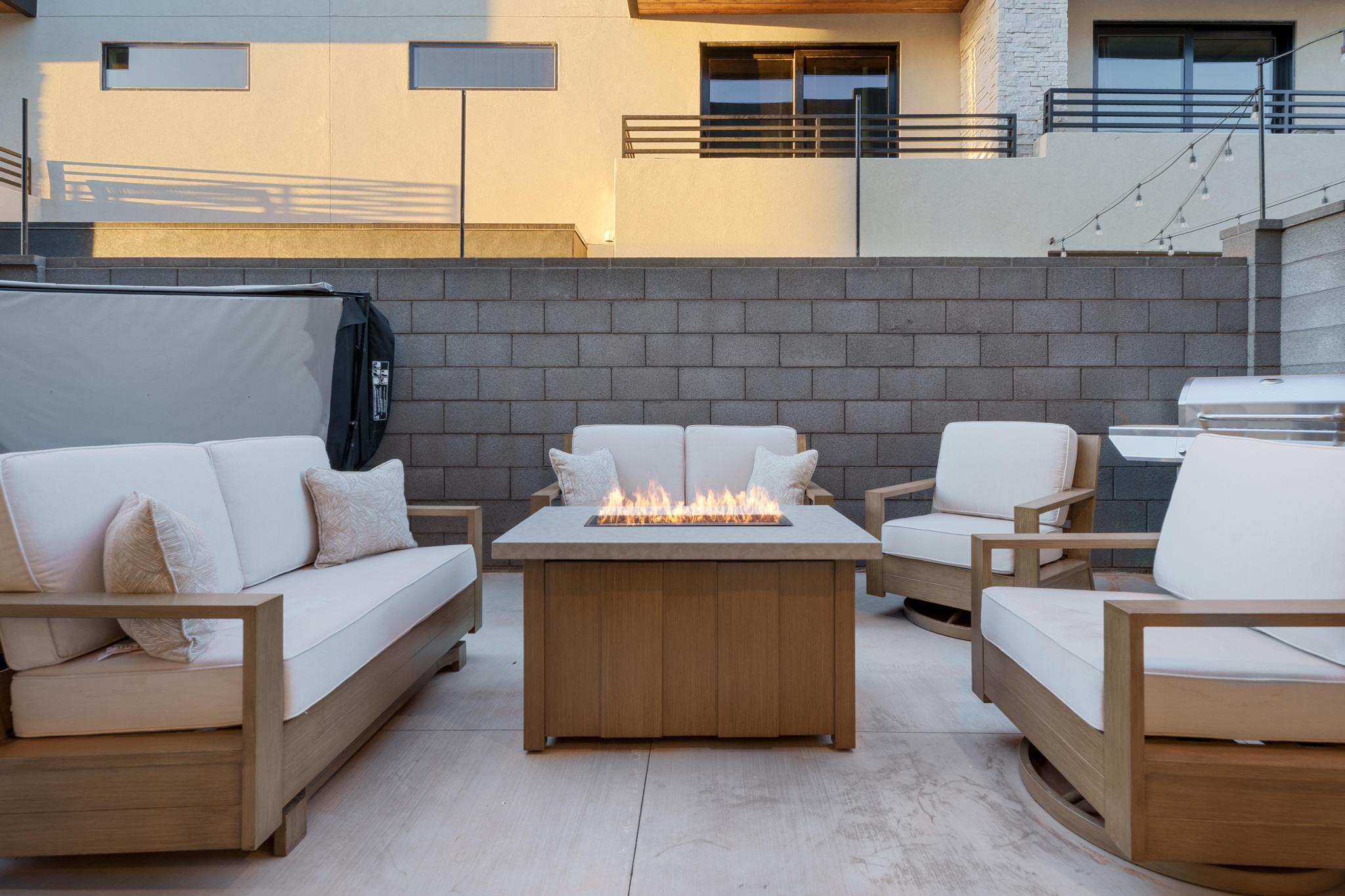 Outdoor patio featuring a built-in fire pit table, string lighting, and a block retaining wall