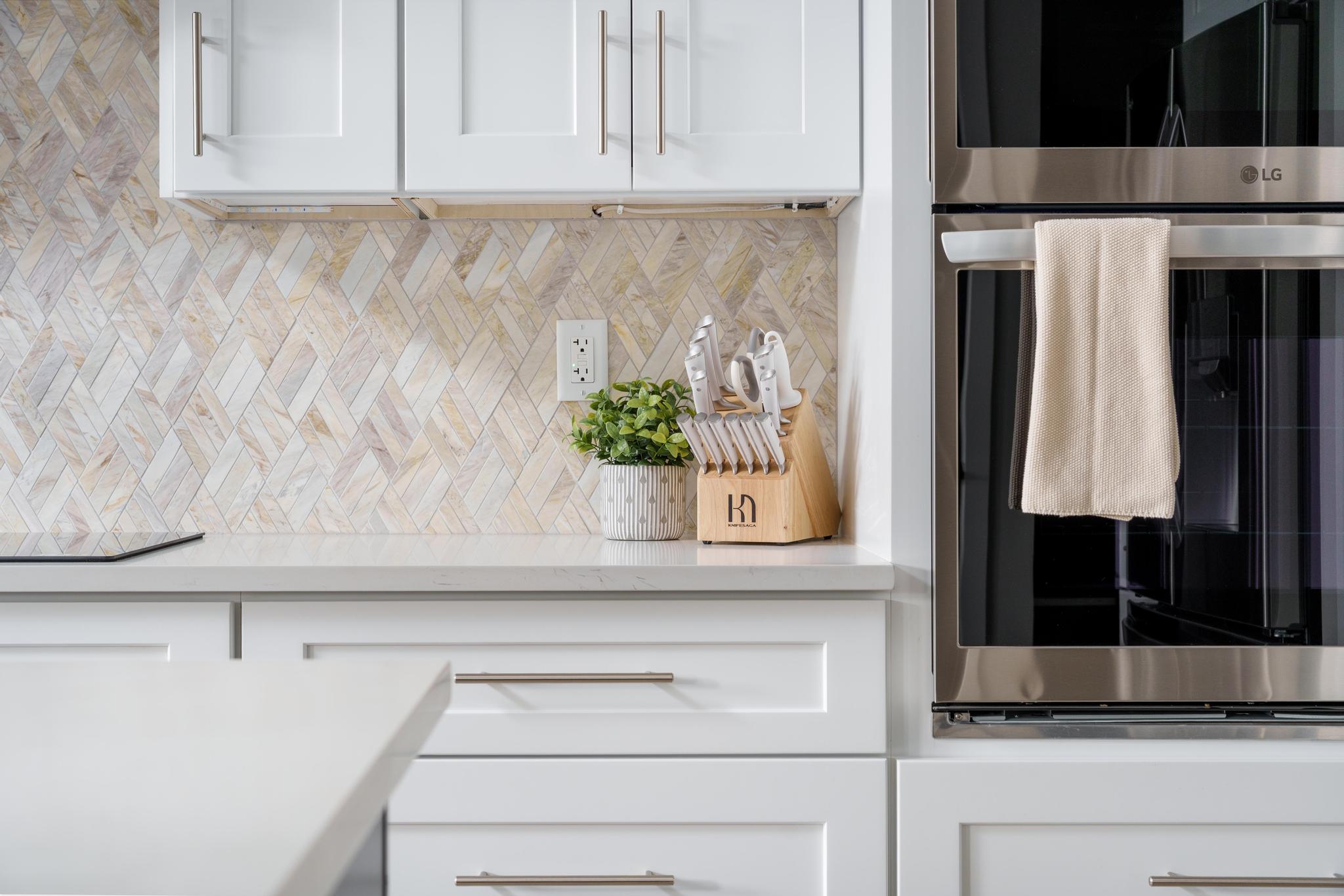 White shaker-style cabinetry with brushed nickel hardware, light-toned countertop, and full-height herringbone pattern tile backsplash