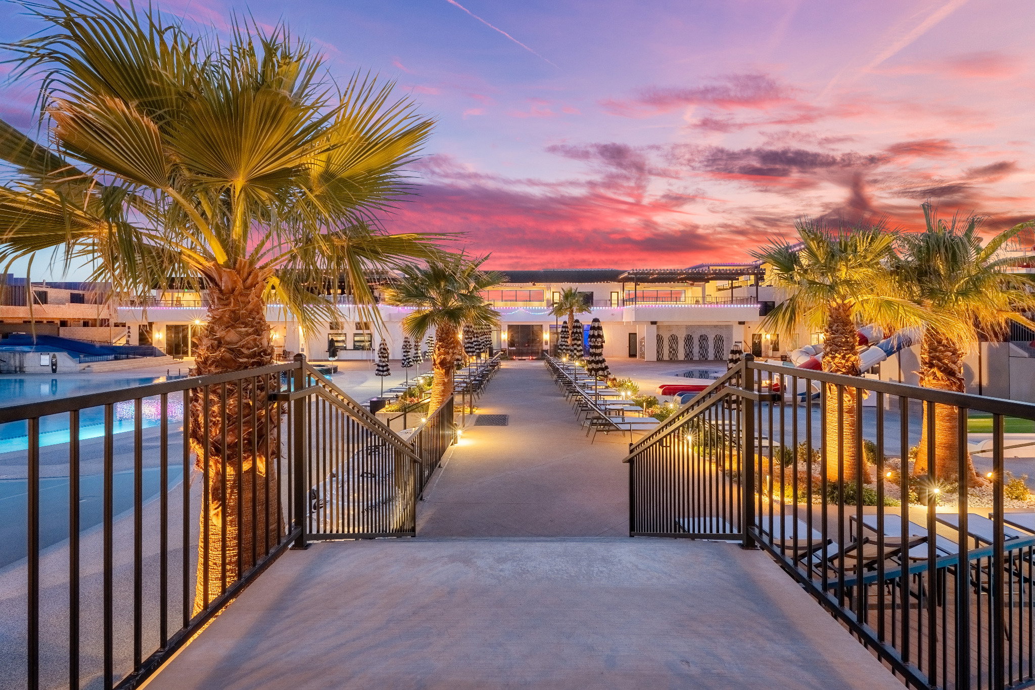 Outdoor leisure area featuring a broad concrete walkway with integrated lighting, flanked by dark metal railings