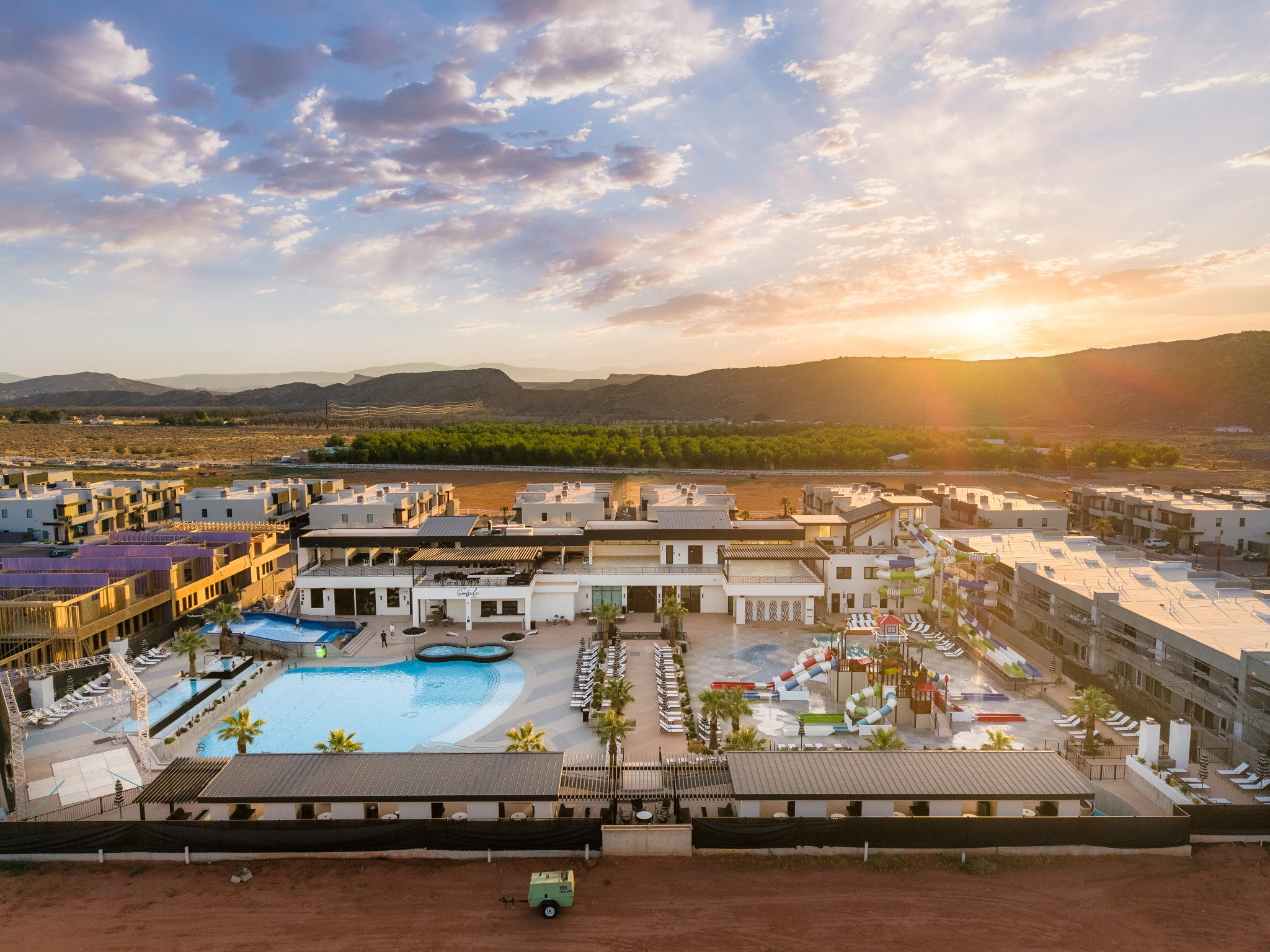 Expansive community pool area featuring a large freeform swimming pool, multiple water slides, numerous lounge chairs, shaded cabanas, and mature palm trees