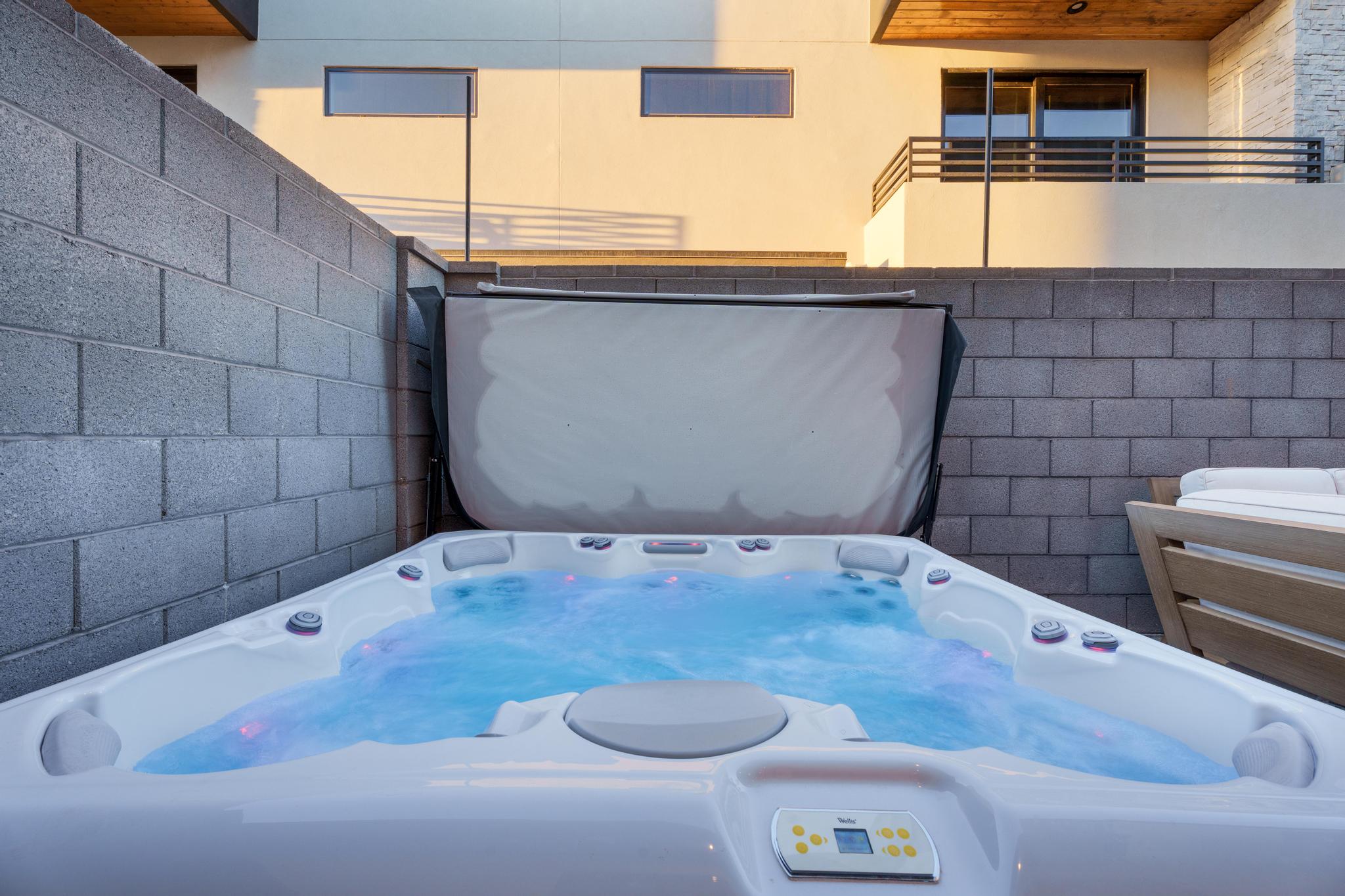 Outdoor spa with integrated lighting, surrounded by block walls, and featuring a privacy cover