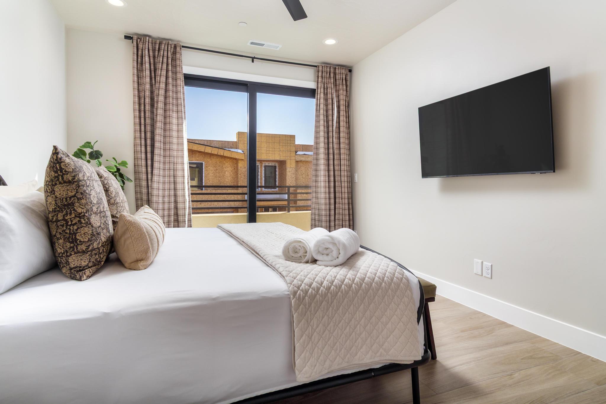 Bedroom featuring a large sliding glass door with balcony access, wood-finish flooring, and a wall-mounted flat-screen television