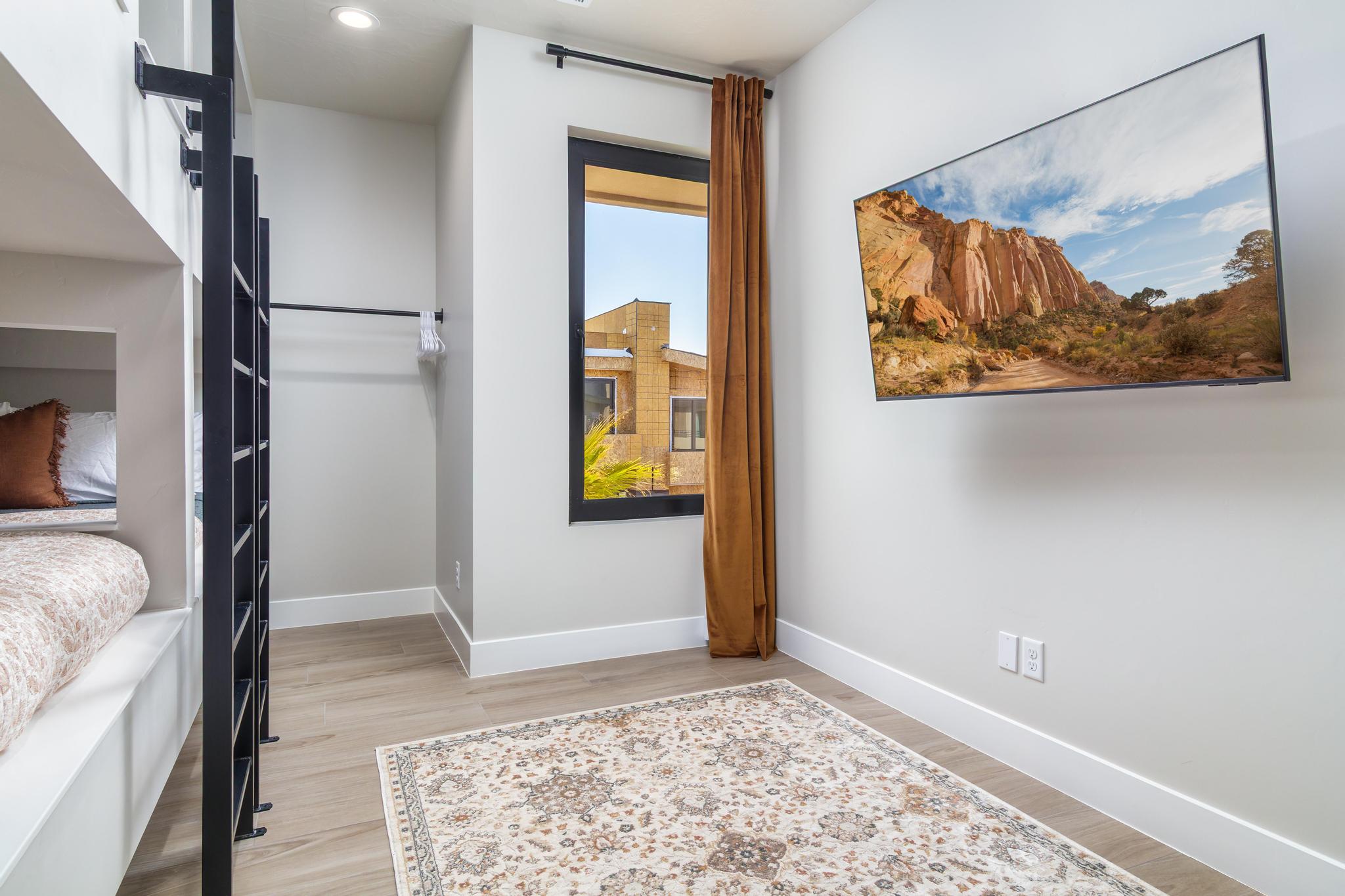 Built-in bunk beds with individual lighting, wood-finish flooring, a contemporary window with brown drapery, and a wall-mounted flat-screen television