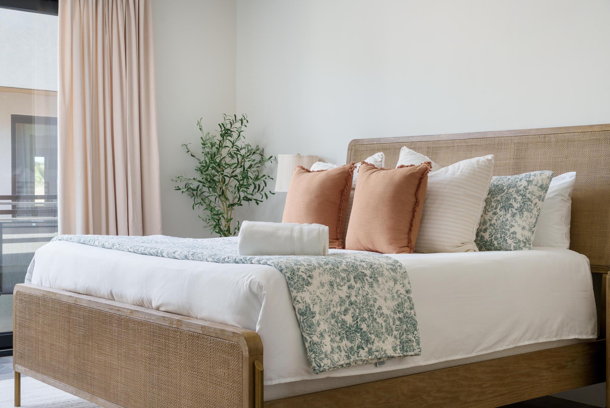 Bright bedroom featuring a woven headboard and footboard, large window with drapes, and light wall finishes